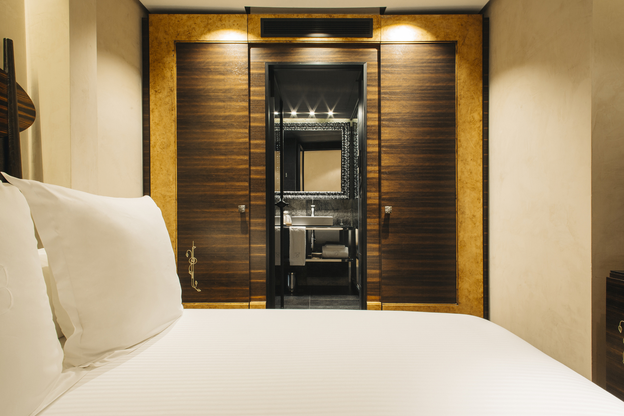 Se ve una cama con almohadas y un pasillo con puerta y marco decorativo de madera oscura.