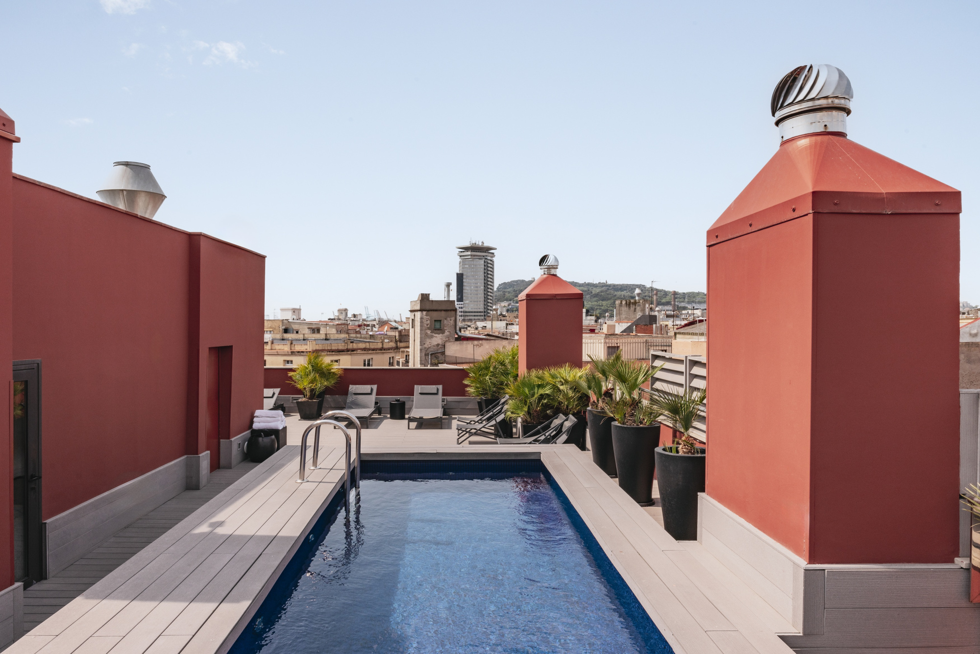 Se ve una piscina exterior rectangular en una terraza con suelo de madera y paredes de color rojo.