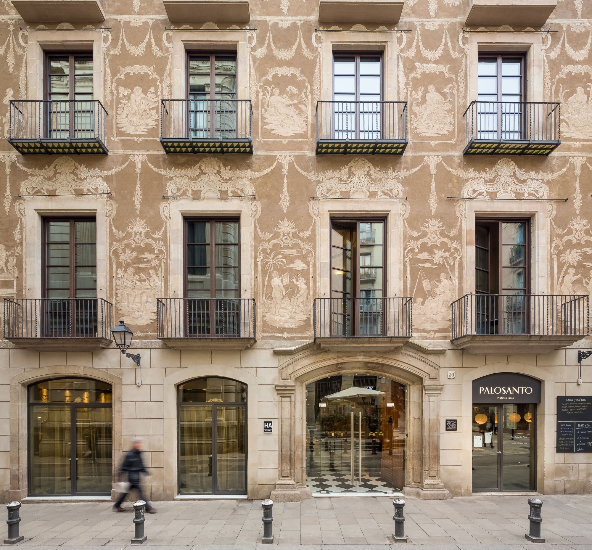 Se ve la fachada de un edificio con balcones y ventanas, además de una entrada con letrero.