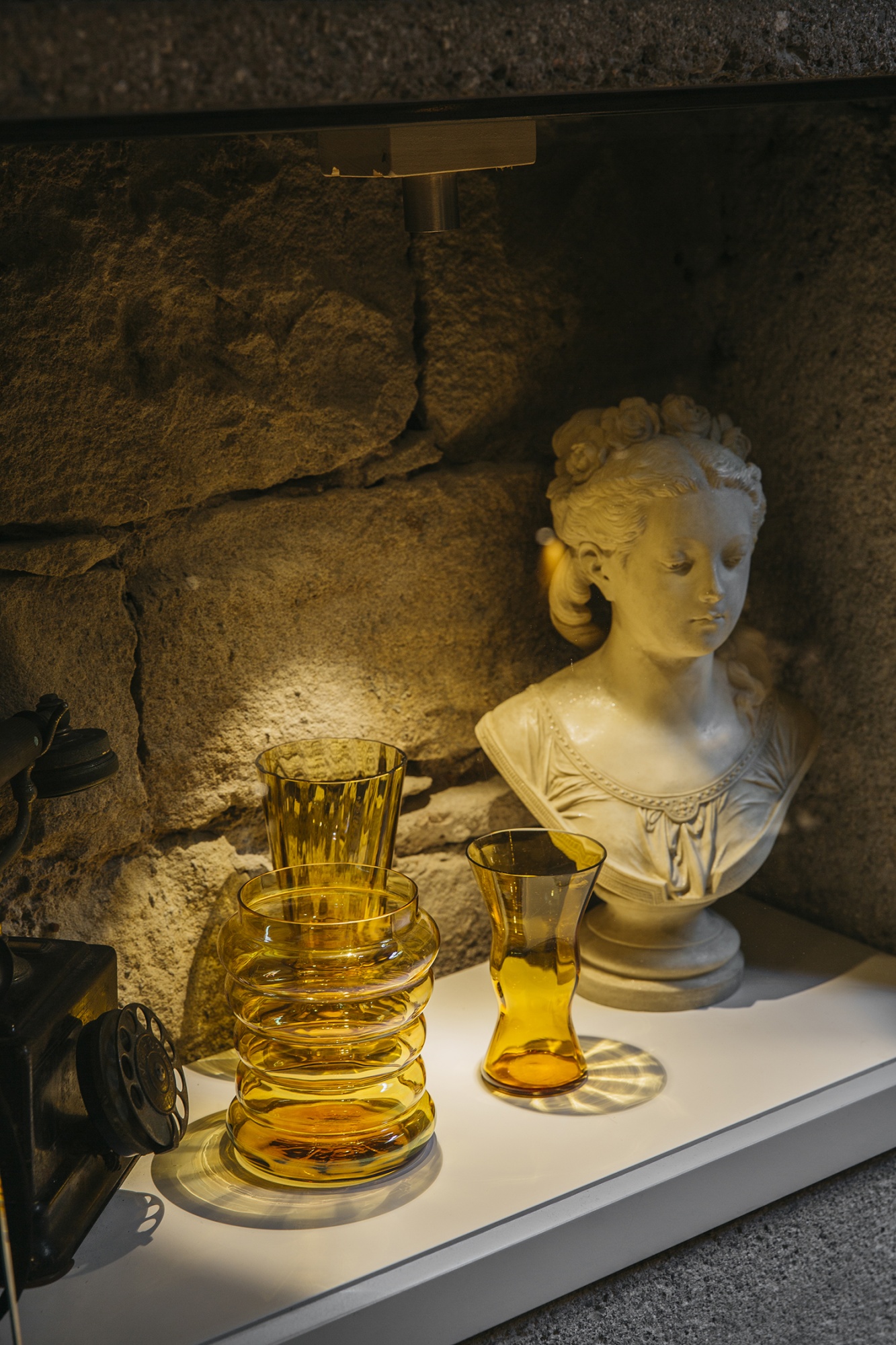 Se ve un busto de mármol sobre una vitrina con dos copas de vidrio y una jarra de cristal.