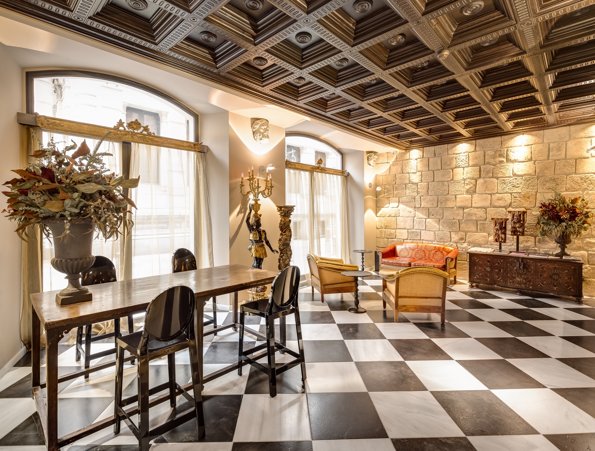 Se ve un vestíbulo con mesa y sillas, una pared de piedra y un sofá junto a ventanas.