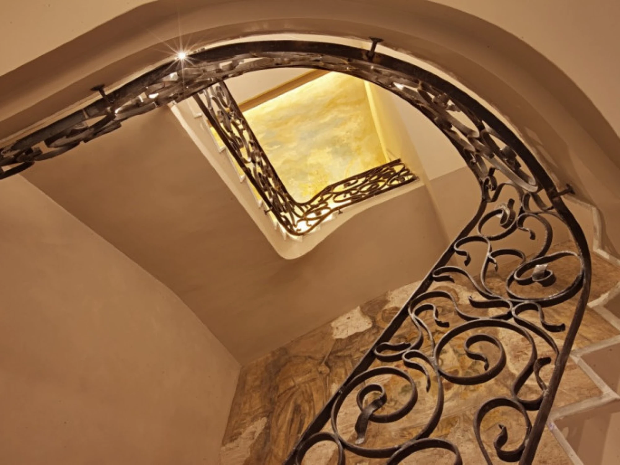 Se ve una escalera interior con barandilla de metal y una pared de piedra al costado.