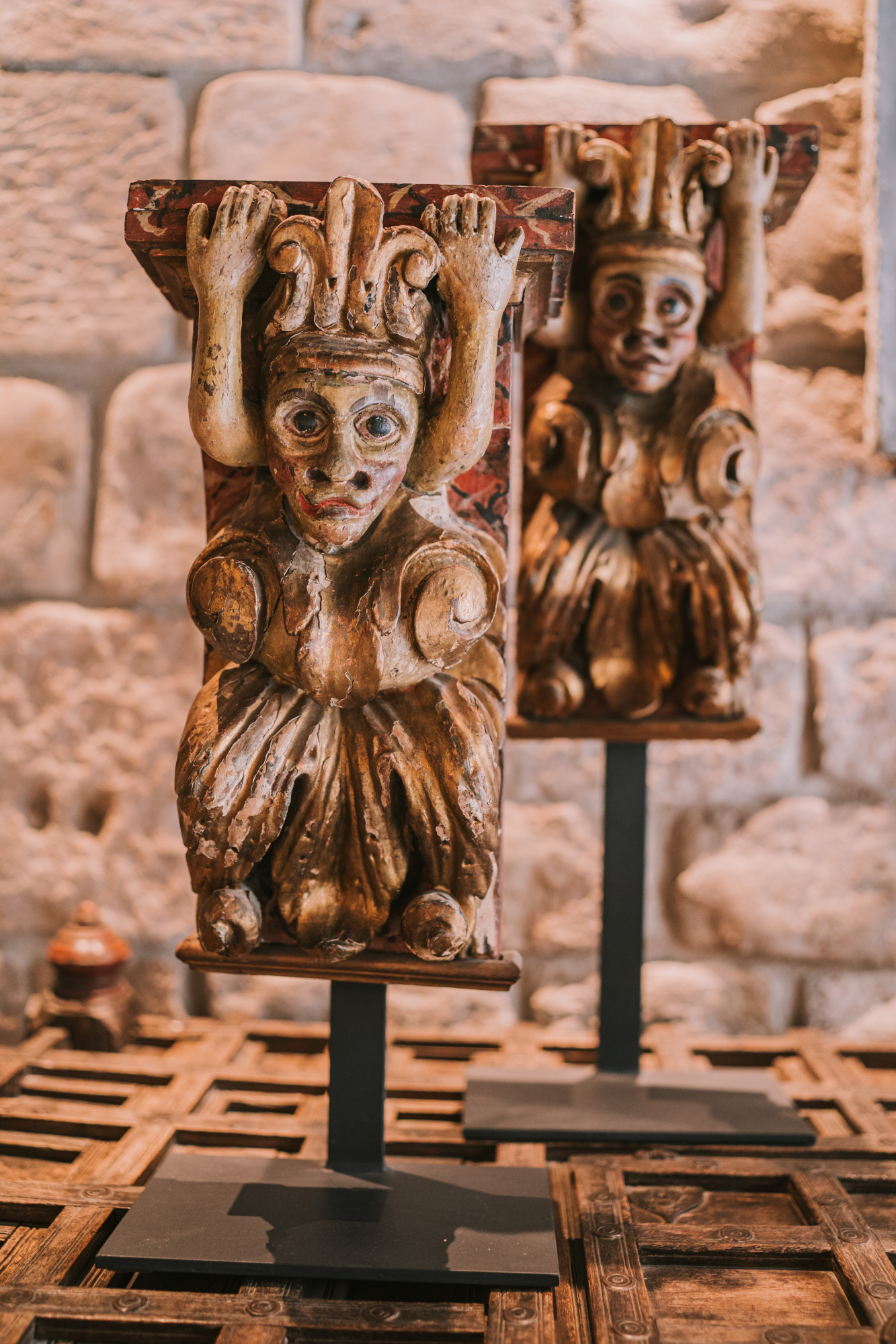 Se observan varias figuras decorativas de madera sobre soportes frente a un muro de piedra.