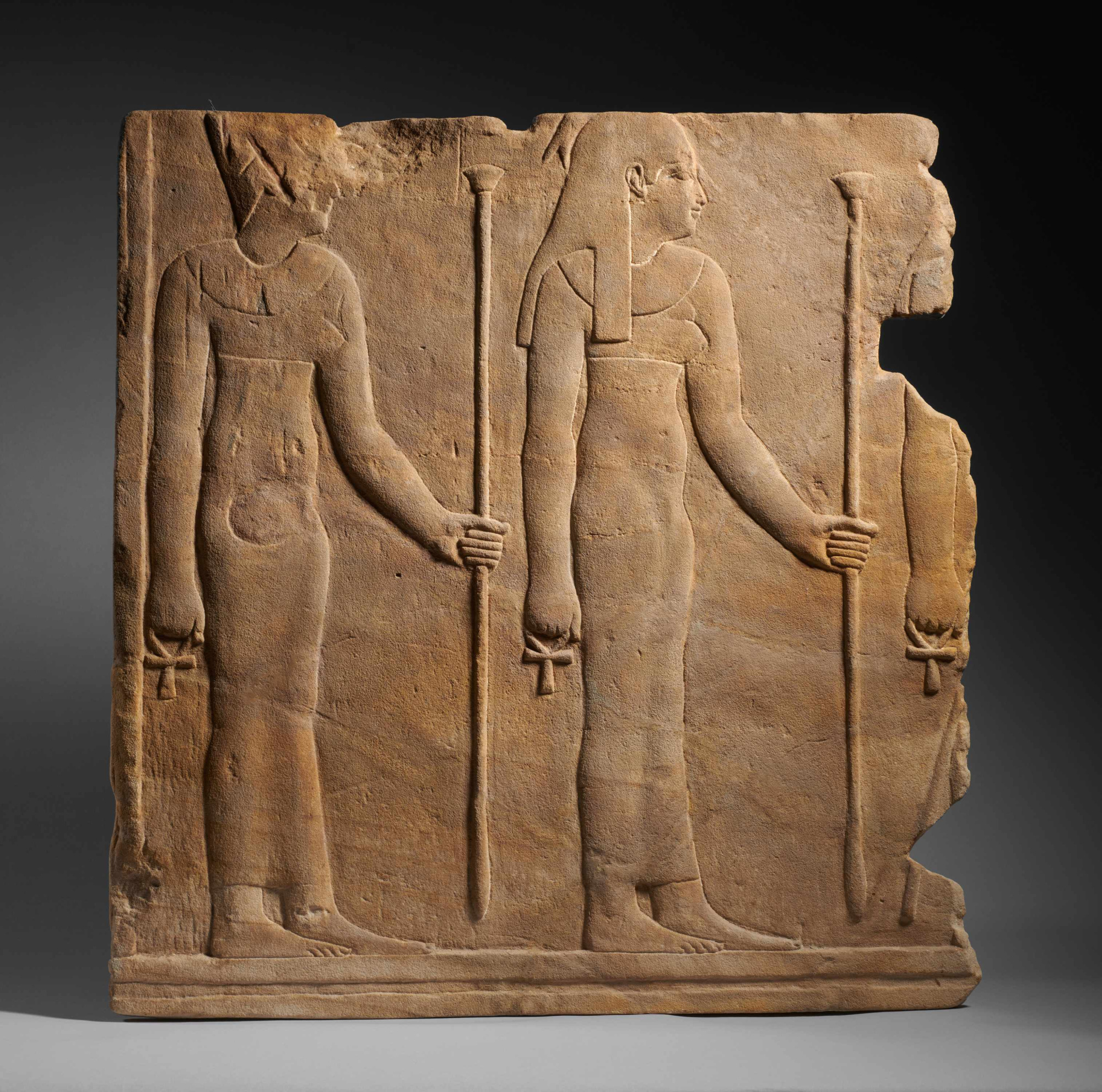 Se ve un relieve de piedra con dos figuras humanas de pie y herramientas en las manos.