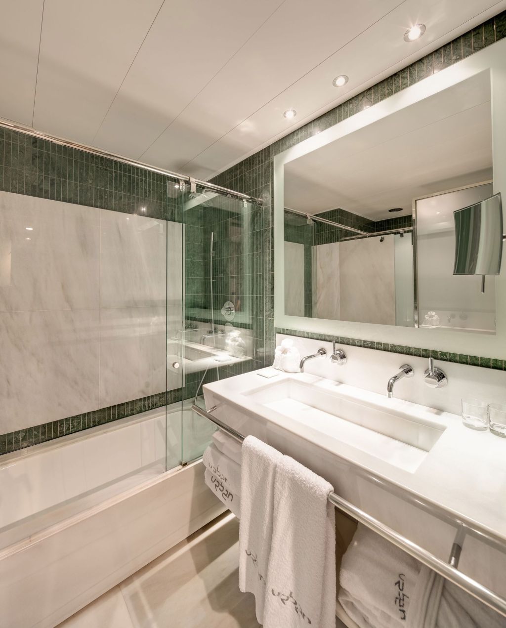 Baño moderno con ducha de vidrio y lavabo doble con encimera blanca.