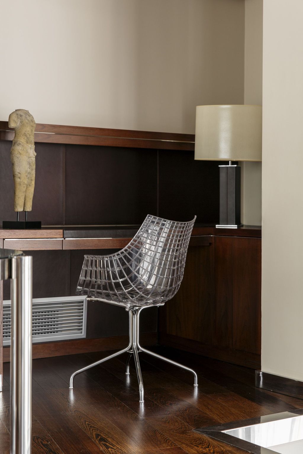 Se ve una silla de metal con cojín sobre suelo de madera junto a una pared con paneles y una lámpara de pie.