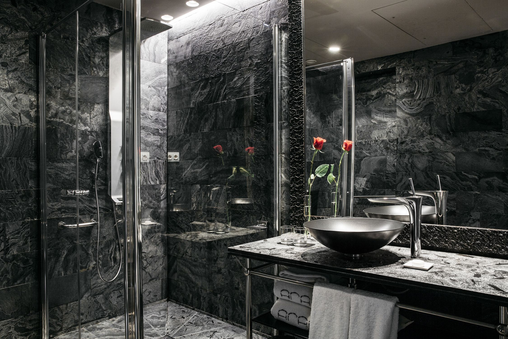 Baño moderno con ducha de cristal, lavabo negro y paredes de piedra oscura.