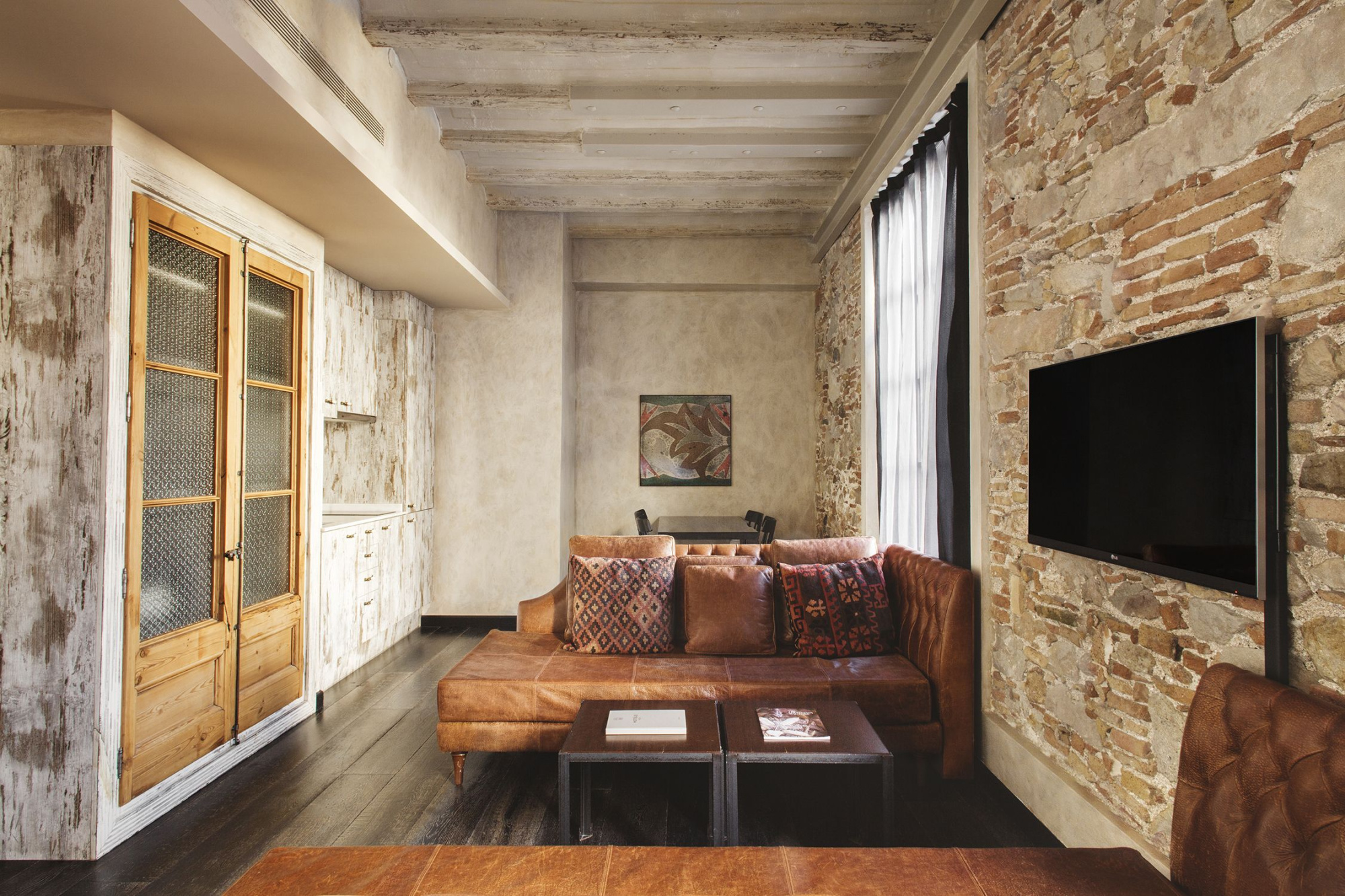 Se ve una sala de estar con sofá, mesa de centro, televisión y paredes de ladrillo visto.