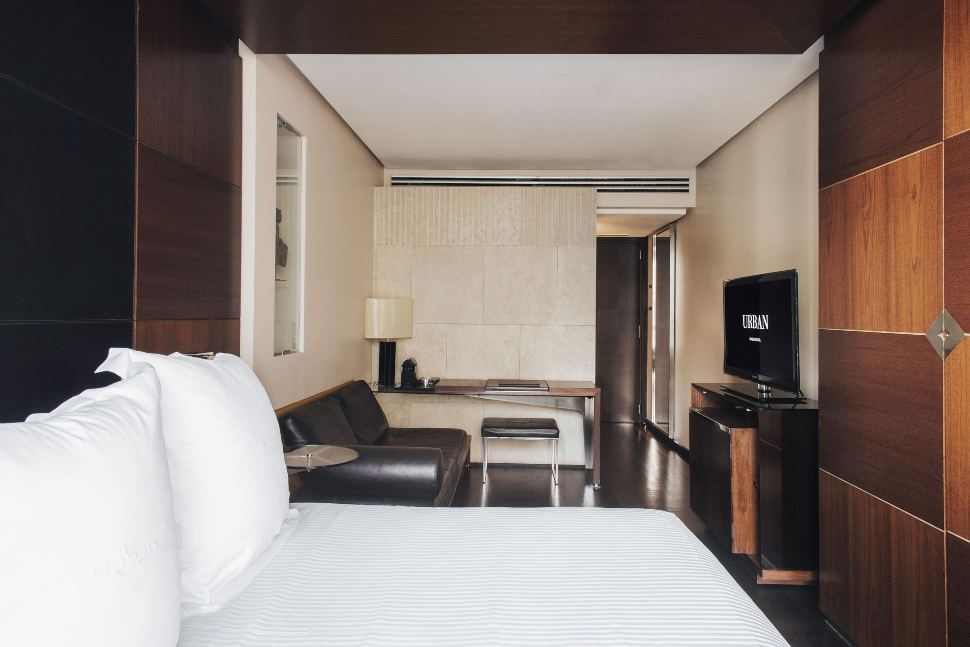 Se ve una cama con almohadas, un sillón y una zona de estar con mesa junto a una pared de madera.