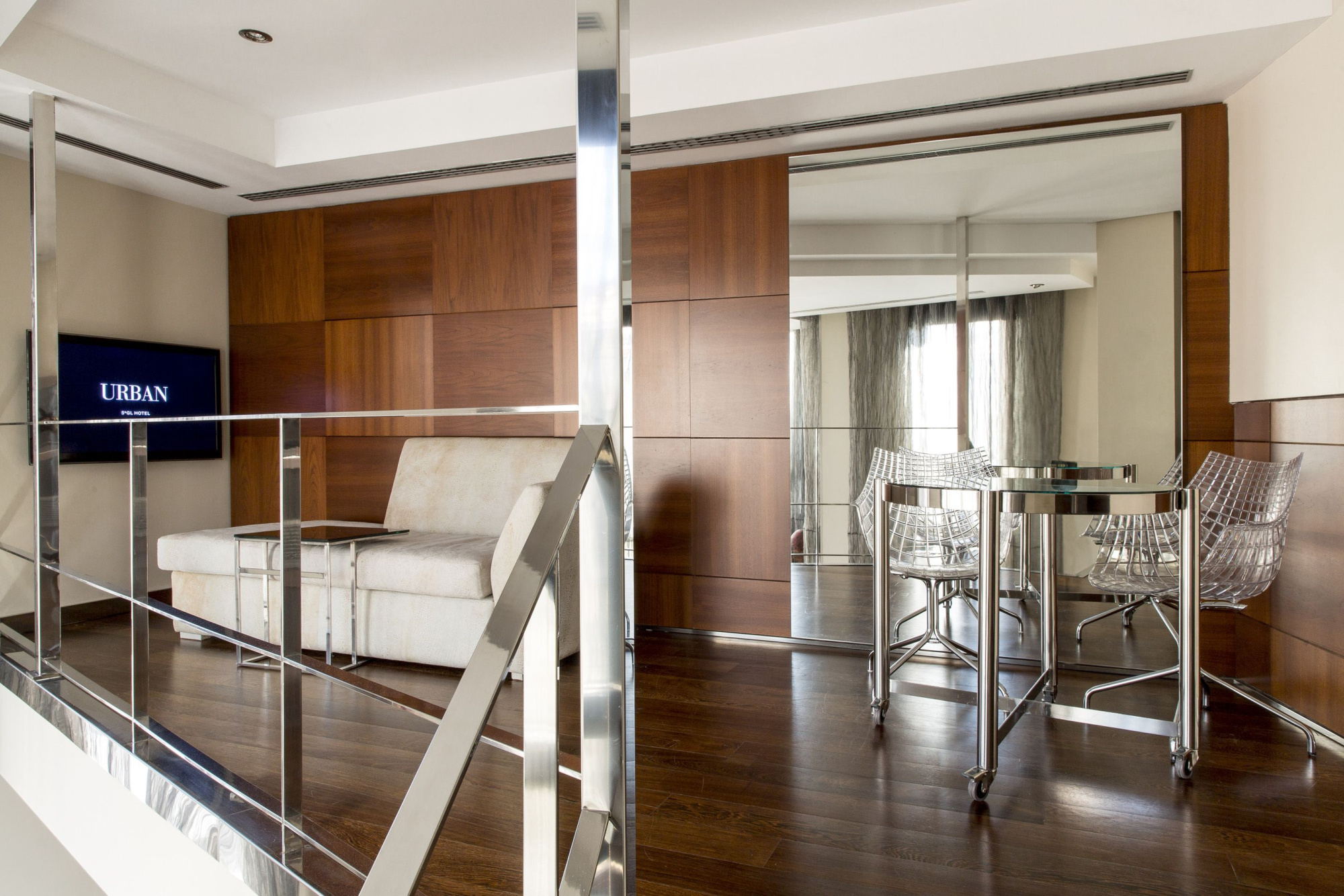 Se ve una zona interior con muebles de madera, una barra alta y taburetes junto a una sala de estar.
