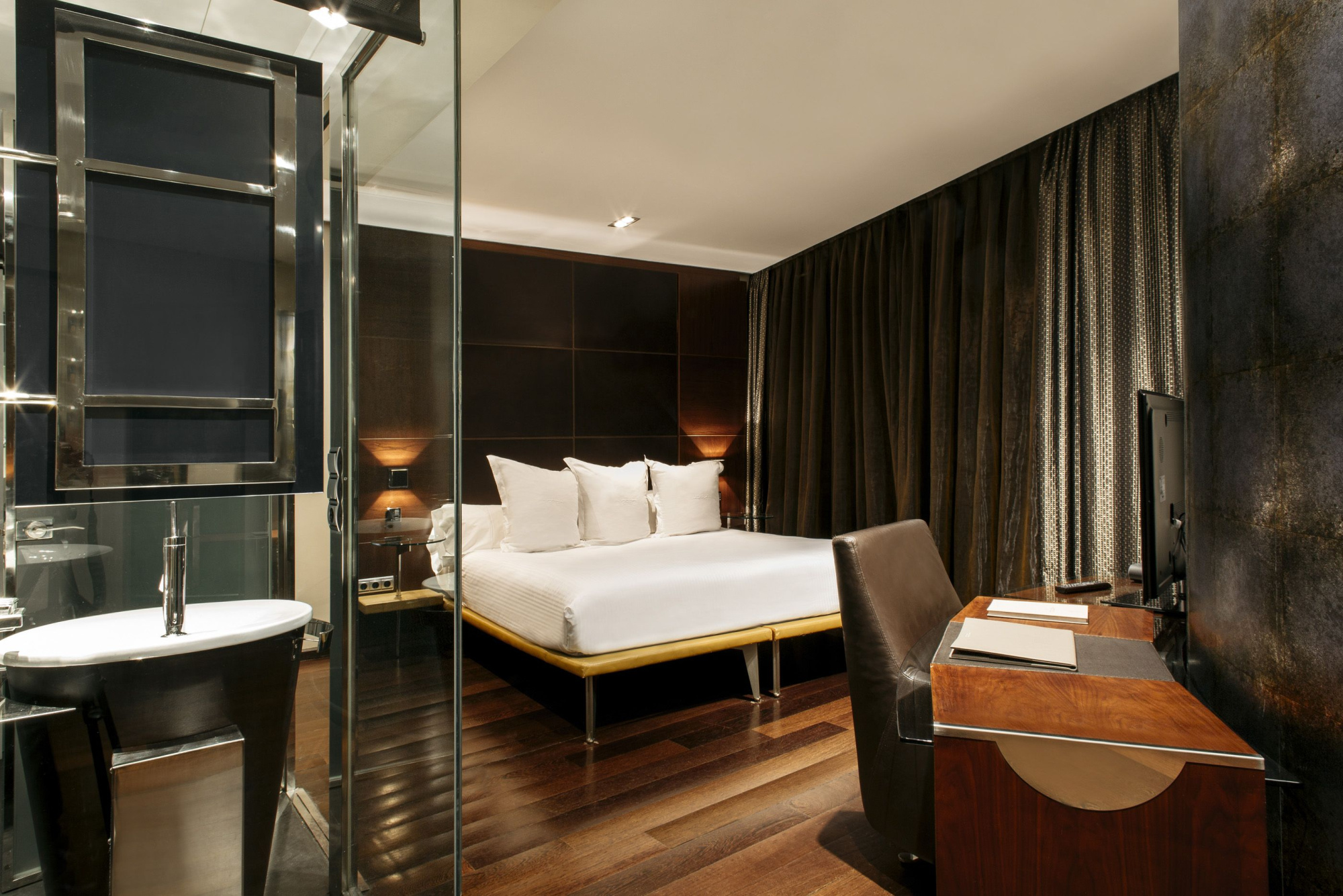 Se ve una habitación con cama doble, escritorio y un baño con lavabo y espejo.