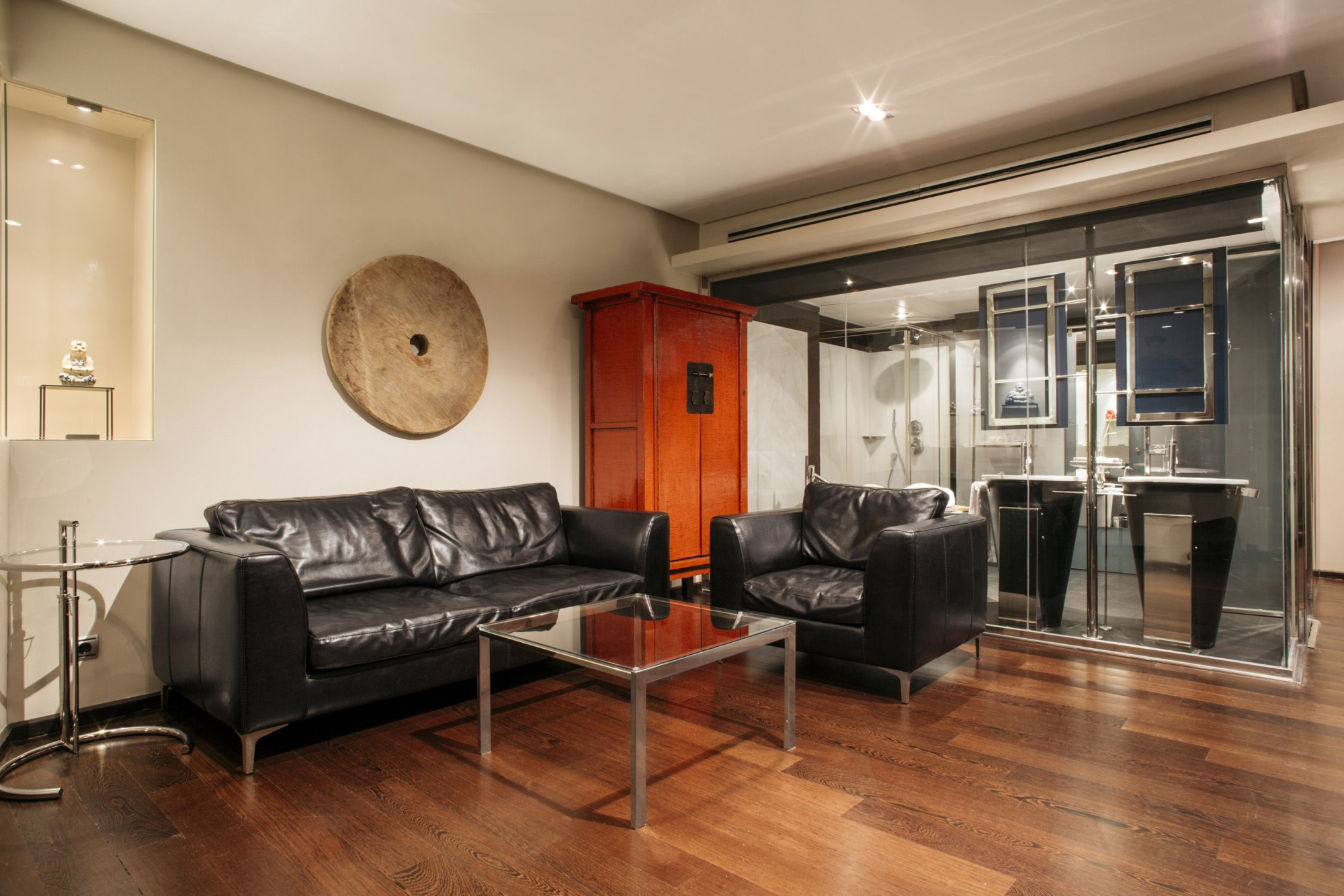 Se ve una sala con dos sillones de cuero, una mesa de centro y suelo de madera junto a una puerta de vidrio.