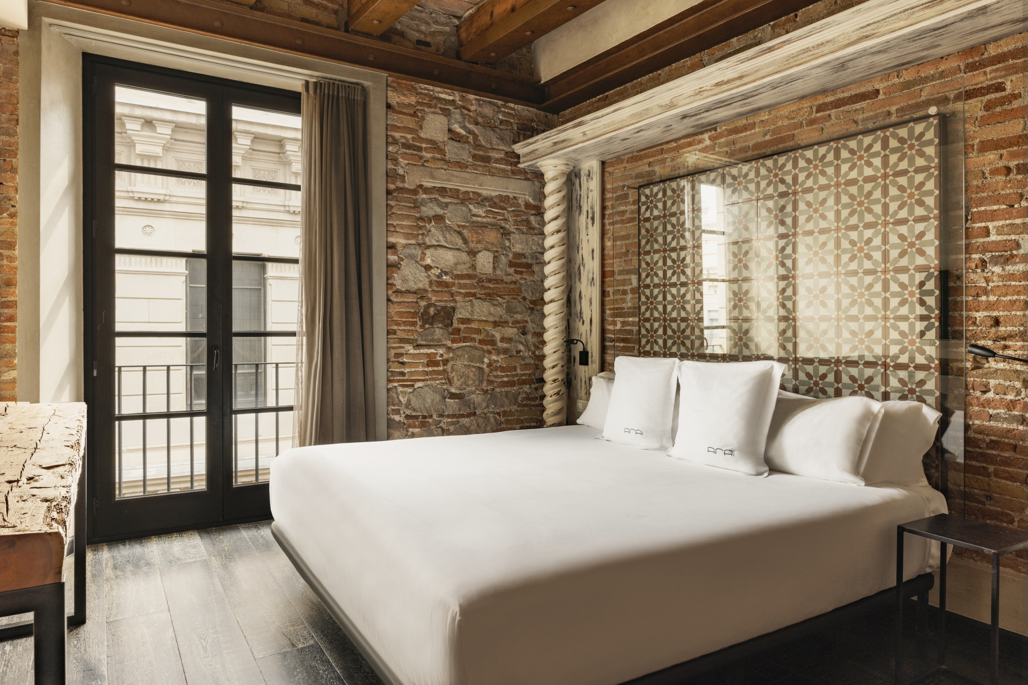 Dormitorio con cama doble, pared de ladrillo visto y puerta con acceso a un balcón.