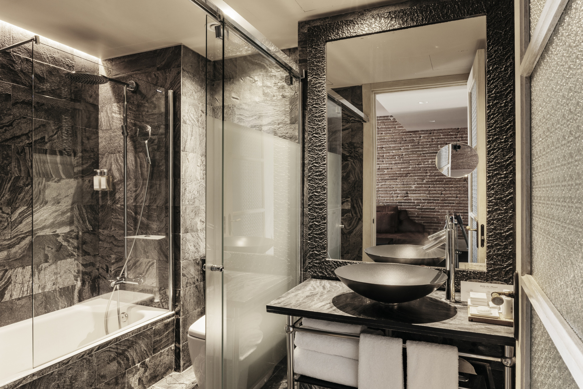 Baño moderno con lavabo negro, ducha con mampara de vidrio y bañera empotrada.