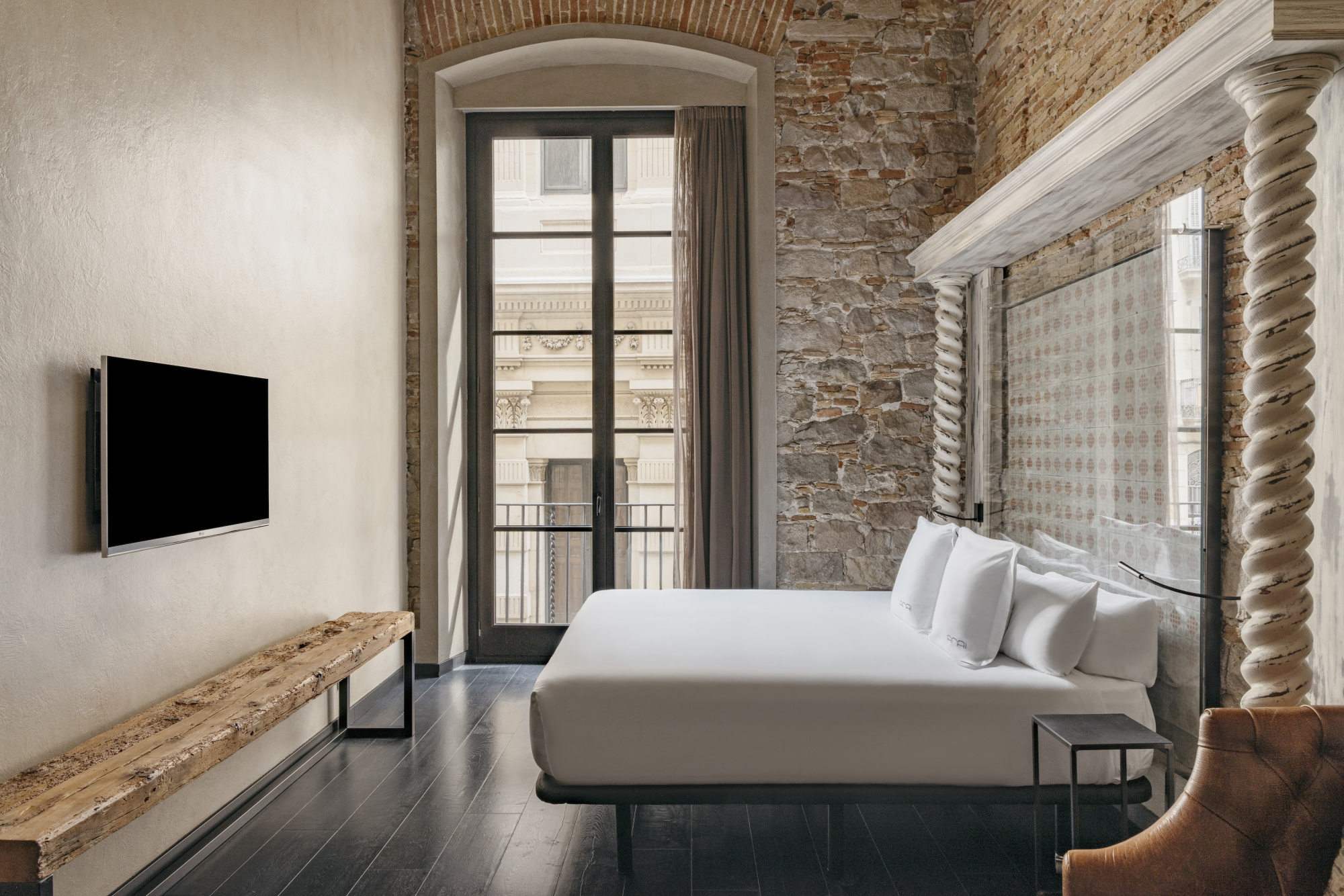 Se ve una habitación con una cama, una pared de ladrillo visto y una puerta que da a un balcón.