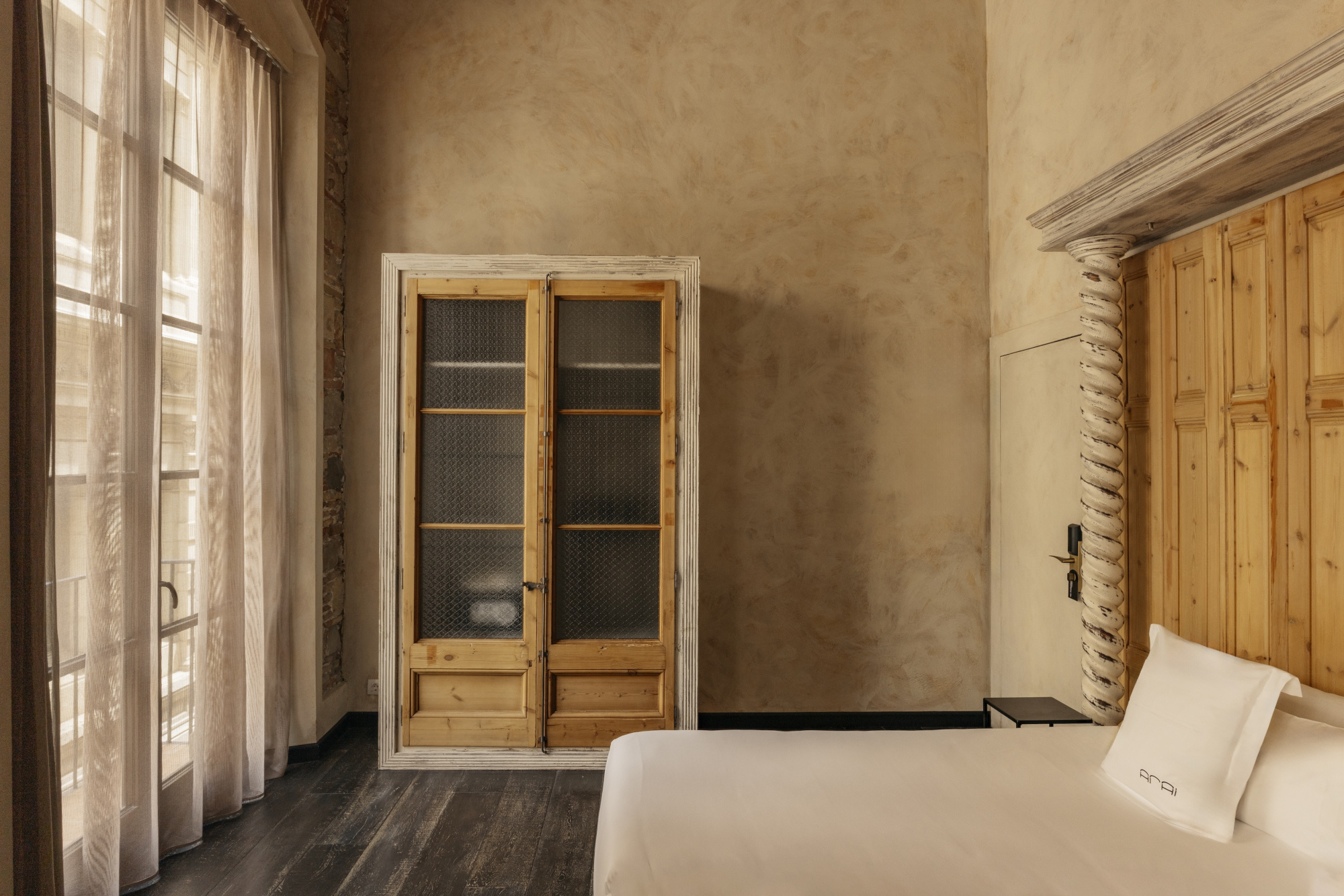 Se ve una cama con almohadas, una vitrina de madera y una ventana con cortinas en una habitación.