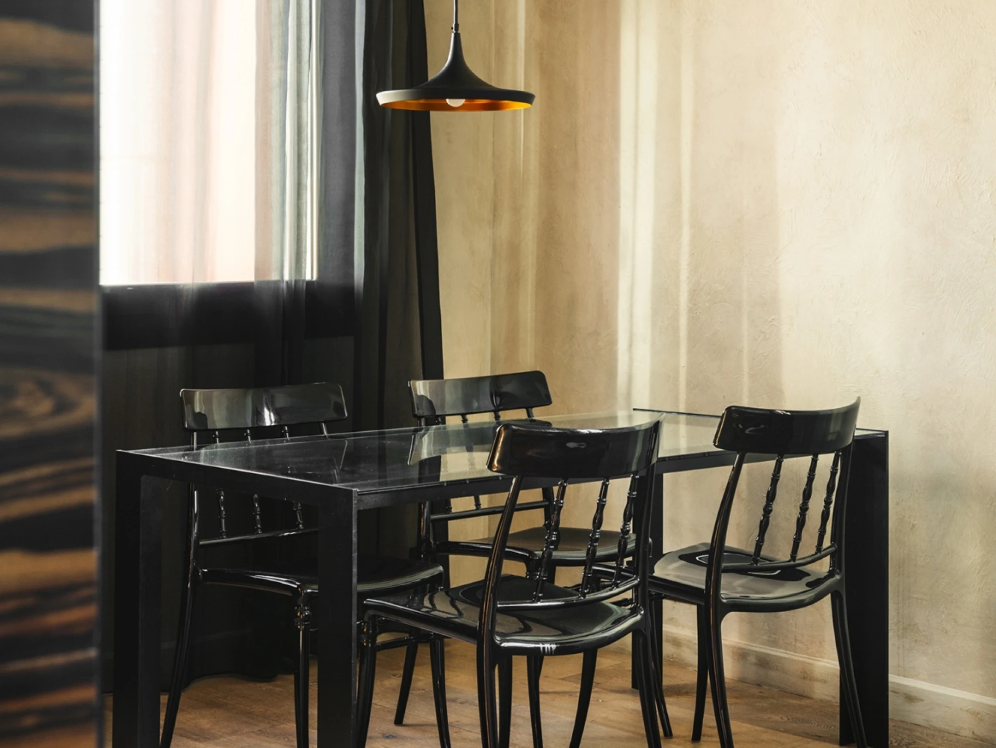 Se ve una mesa de comedor con sillas negras y una lámpara colgante en un espacio interior con paredes claras.