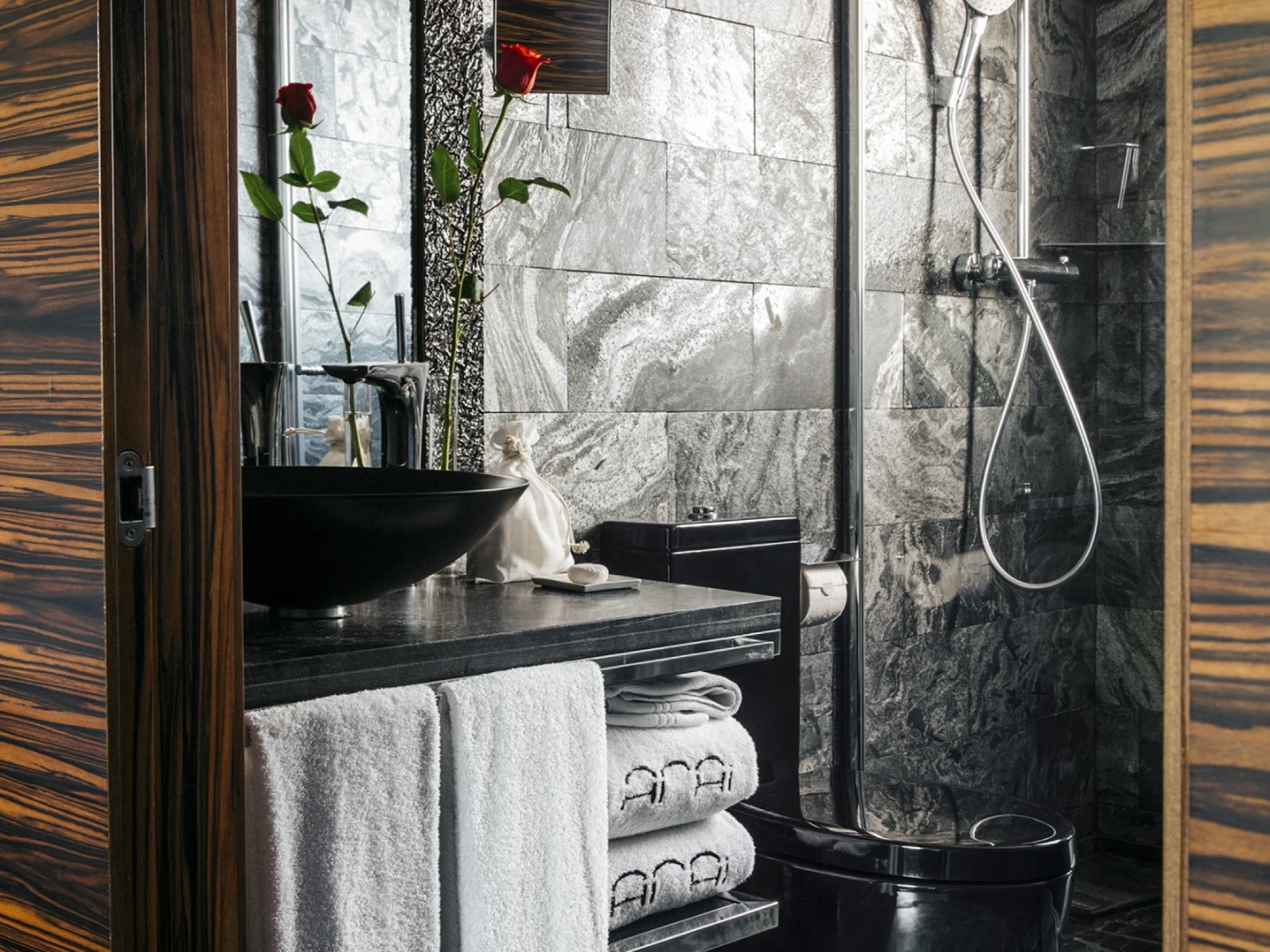Se ve un lavabo negro con toallas y una ducha con mampara de vidrio en un baño moderno.