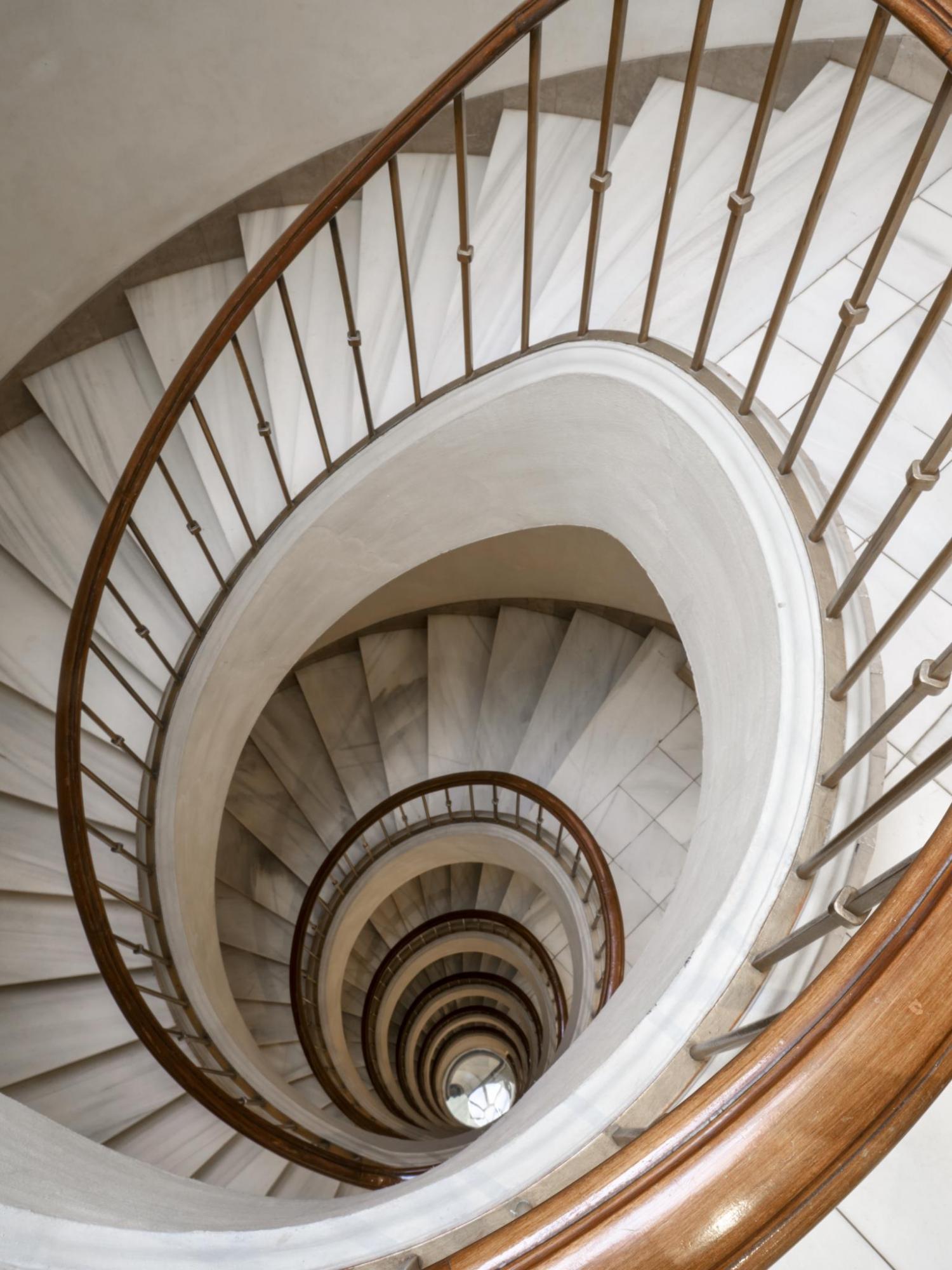 Describe una escalera de caracol interior con barandilla de metal y peldaños de piedra.