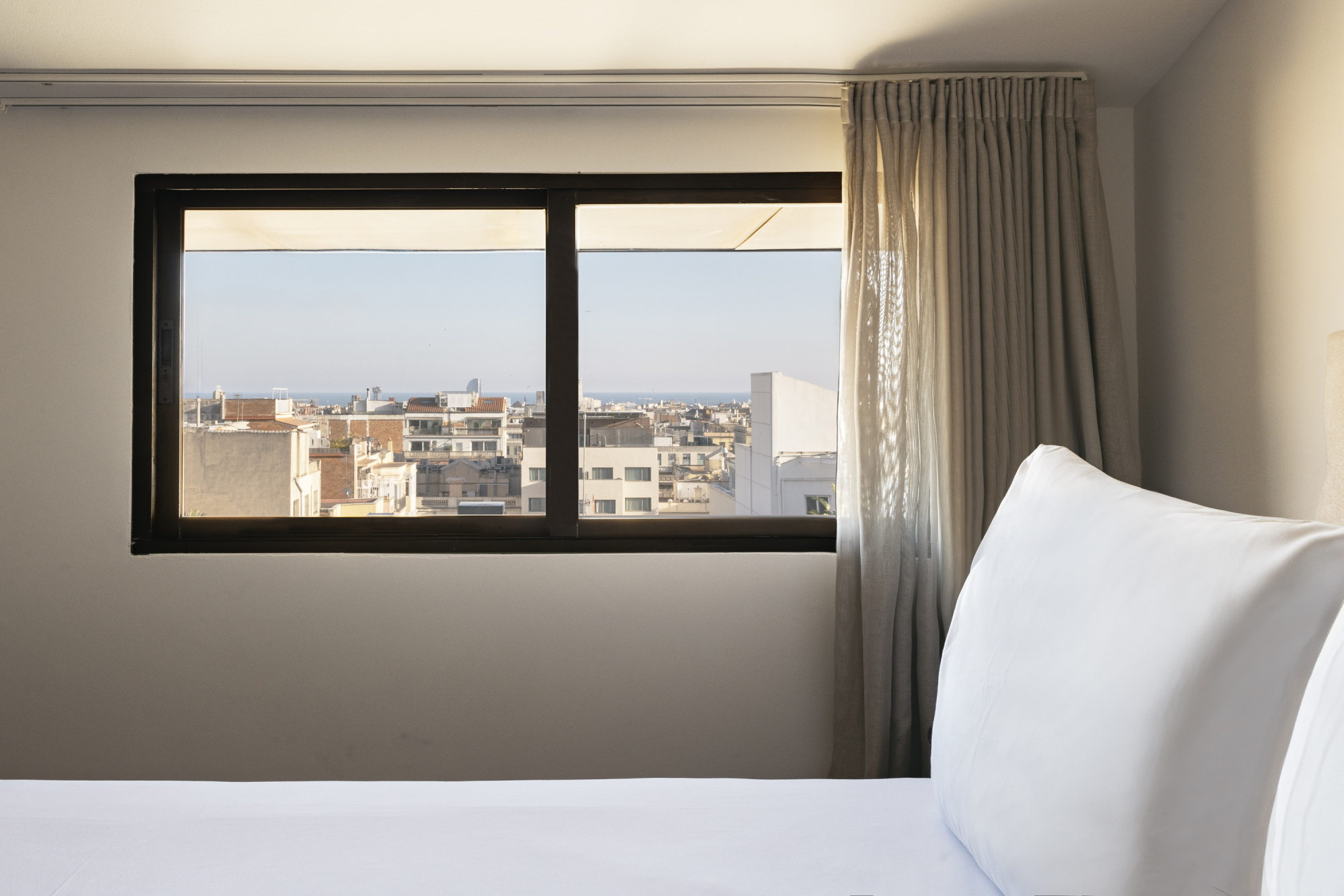 Una habitación de hotel moderna con decoración elegante y colores neutros, que incluye una cama grande, ropa de cama blanca y detalles decorativos en tonos suaves.
