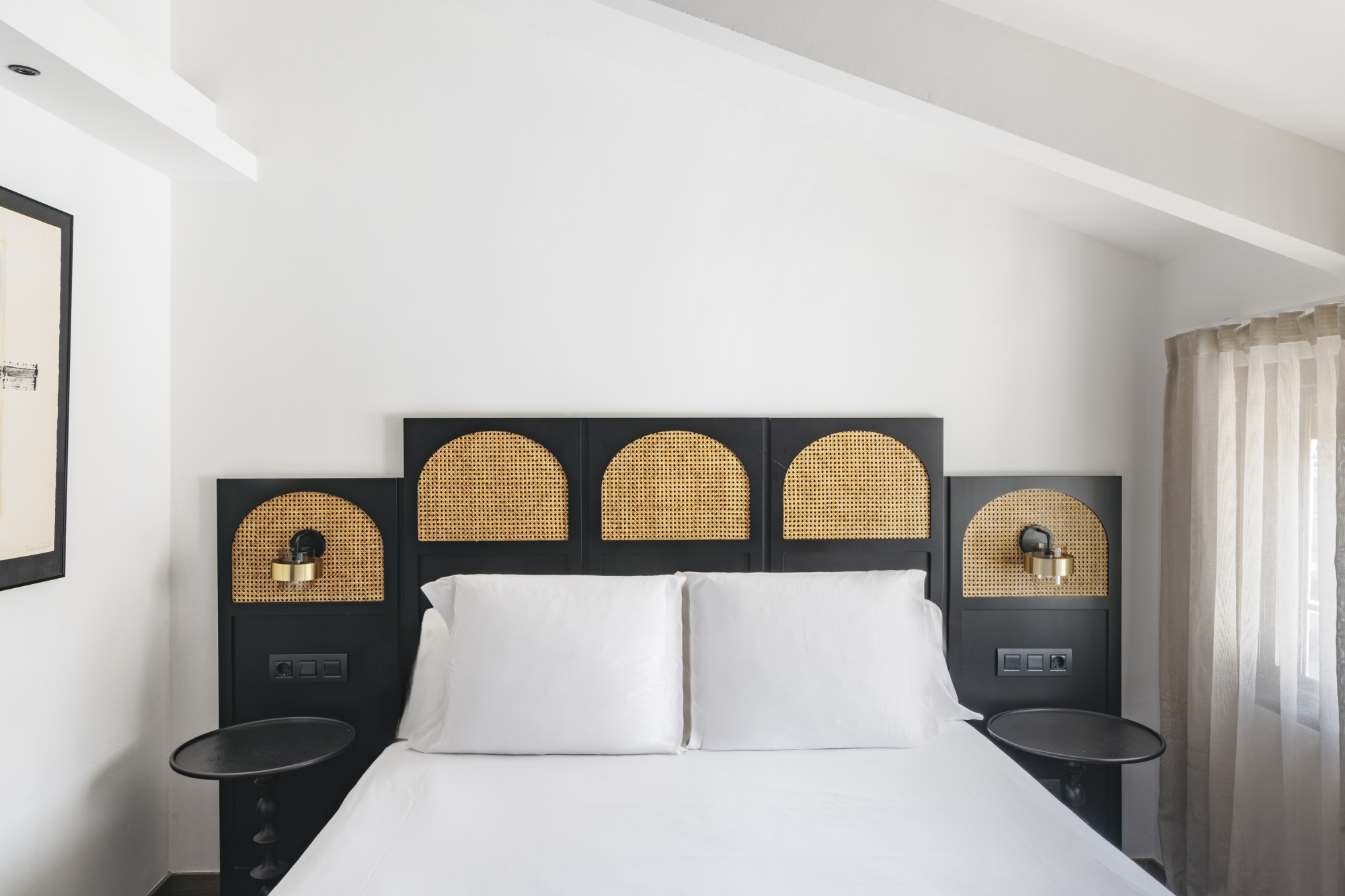 Una habitación de hotel moderna con decoración elegante y colores neutros, que incluye una cama grande, ropa de cama blanca y detalles decorativos en tonos suaves.