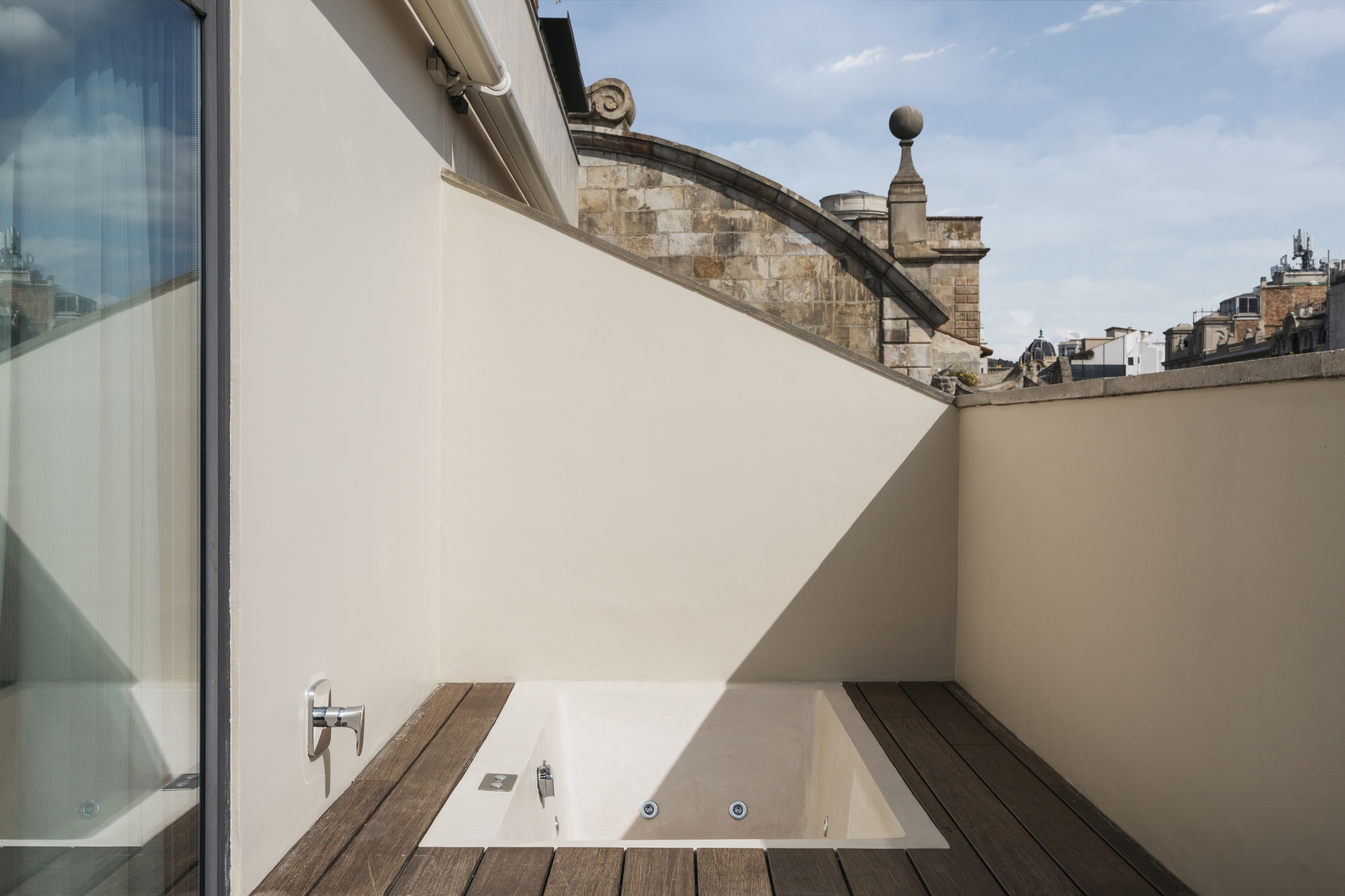 Se ve una terraza estrecha con suelo de madera, paredes claras y una barandilla de metal en un lateral.