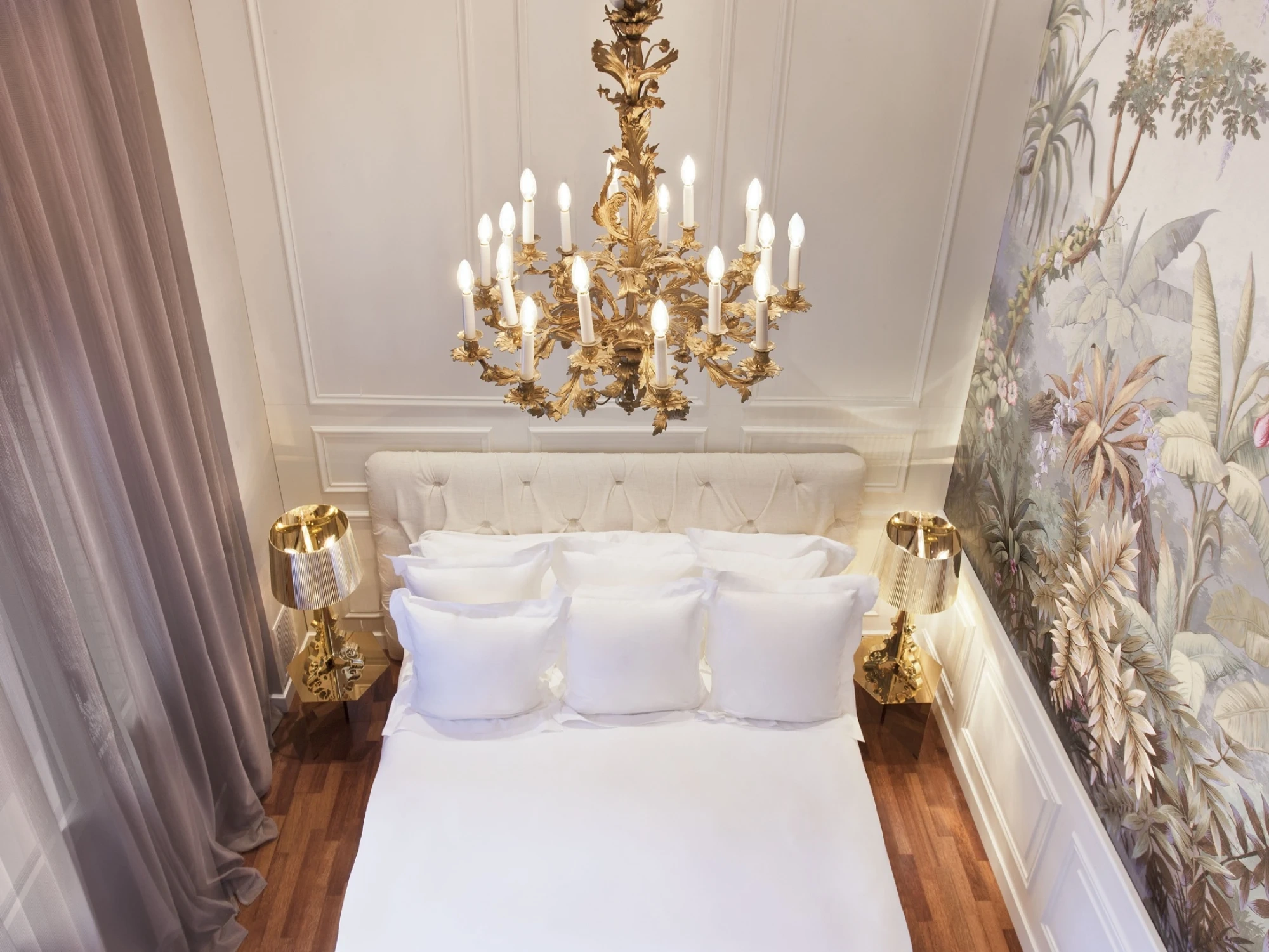 Se ve una cama doble con ropa de cama blanca y dos mesitas laterales junto a cortinas claras.