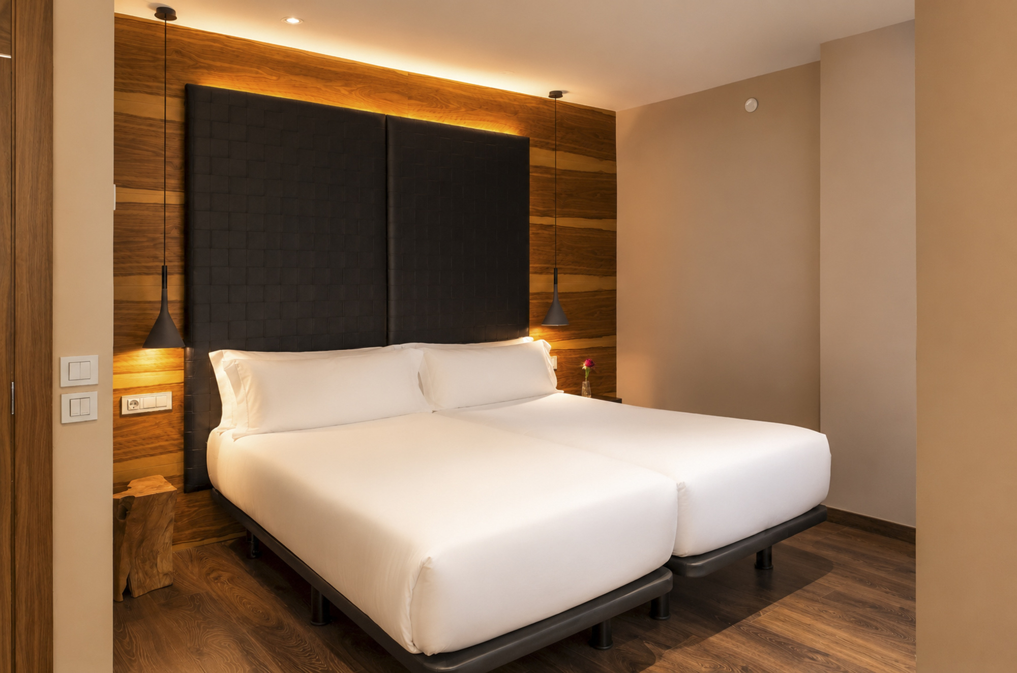 Se ve una cama doble con ropa de cama blanca y una pared con paneles oscuros y luz empotrada.