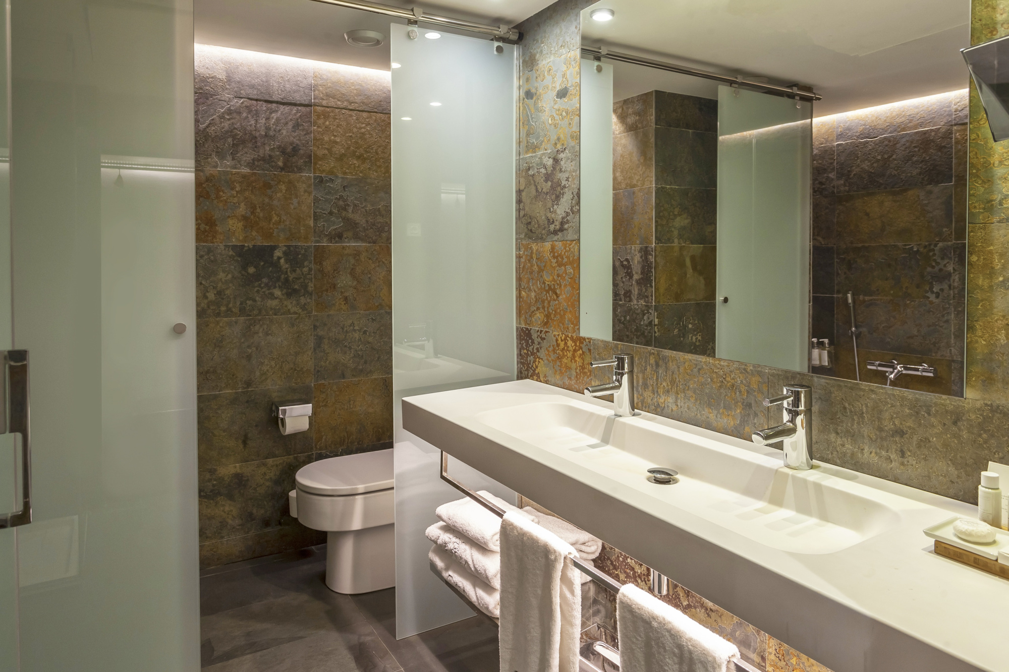 El baño muestra un lavabo doble con encimera clara, grifería cromada, espejo y ducha con mampara de vidrio.