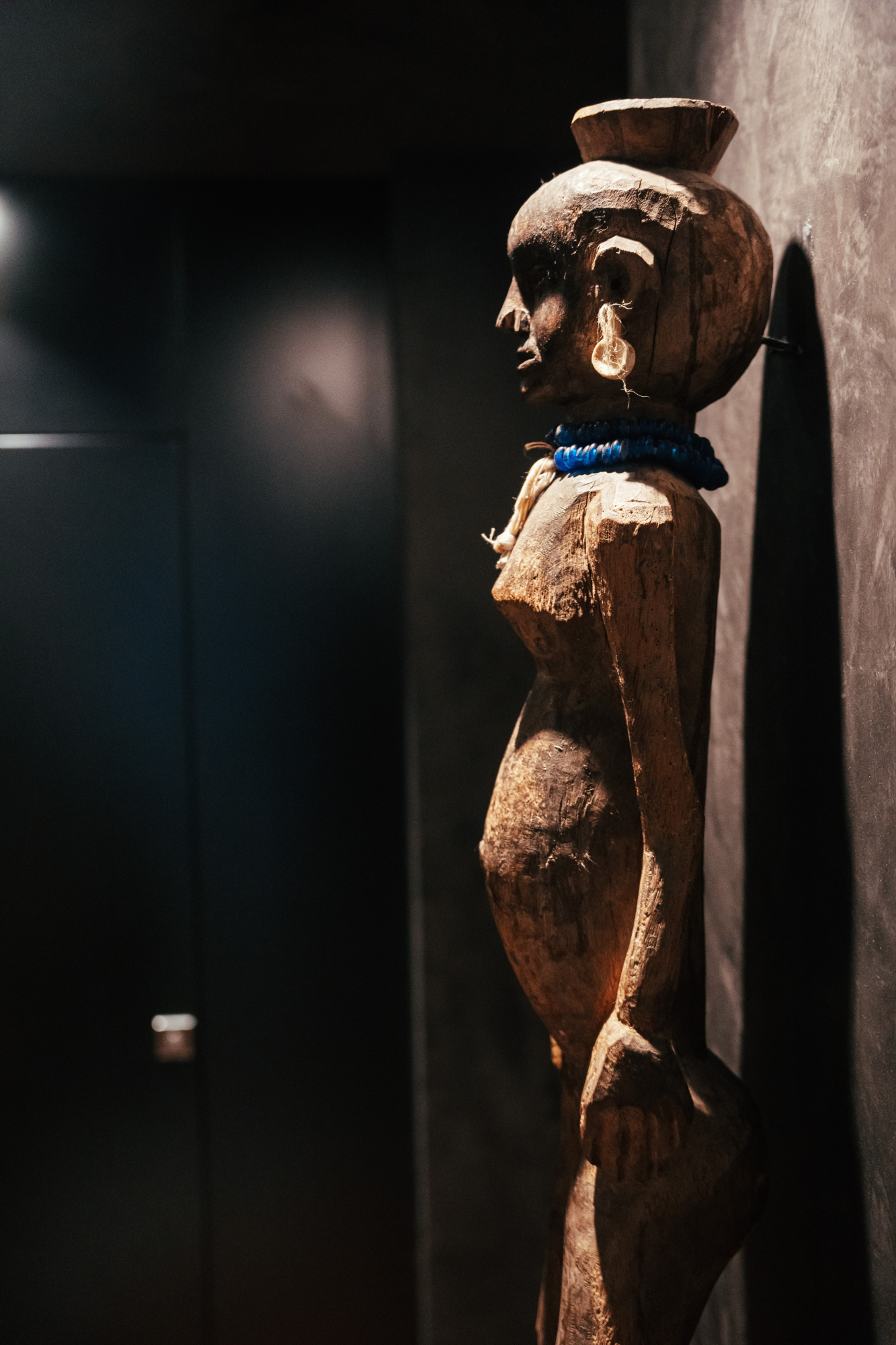 Se ve una escultura decorativa de madera sobre una peana, iluminada con luz tenue en un espacio interior.