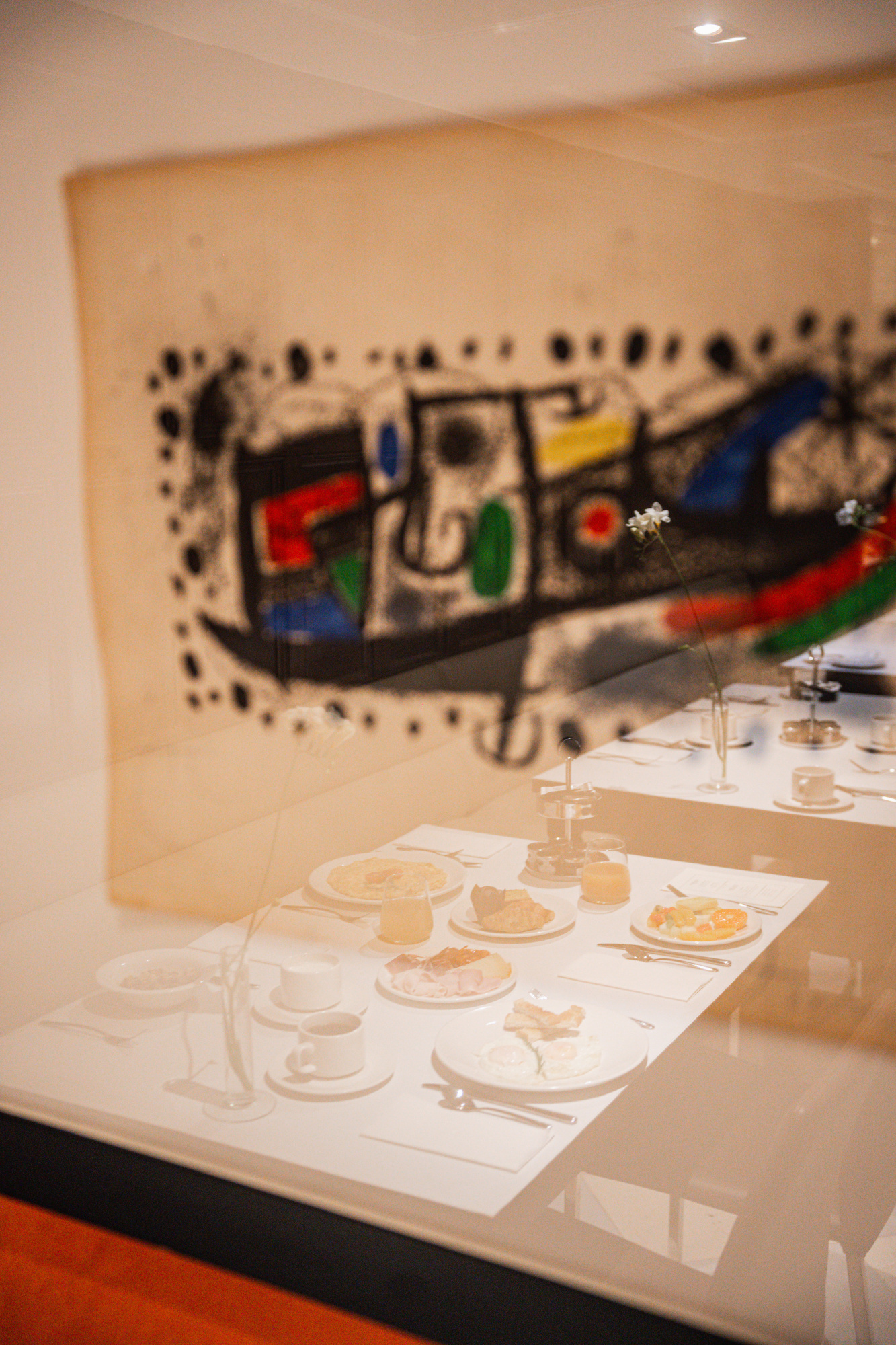 Se ve una mesa con copas y platos sobre un mantel, con un mural artístico en la pared al fondo.