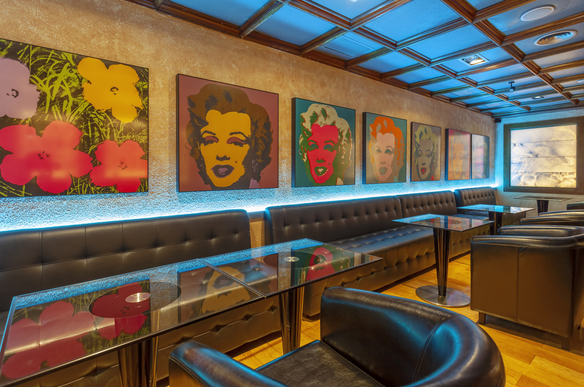 Un bar interior con asientos tapizados, mesas y una pared con cuadros decorativos y luces ambientales.
