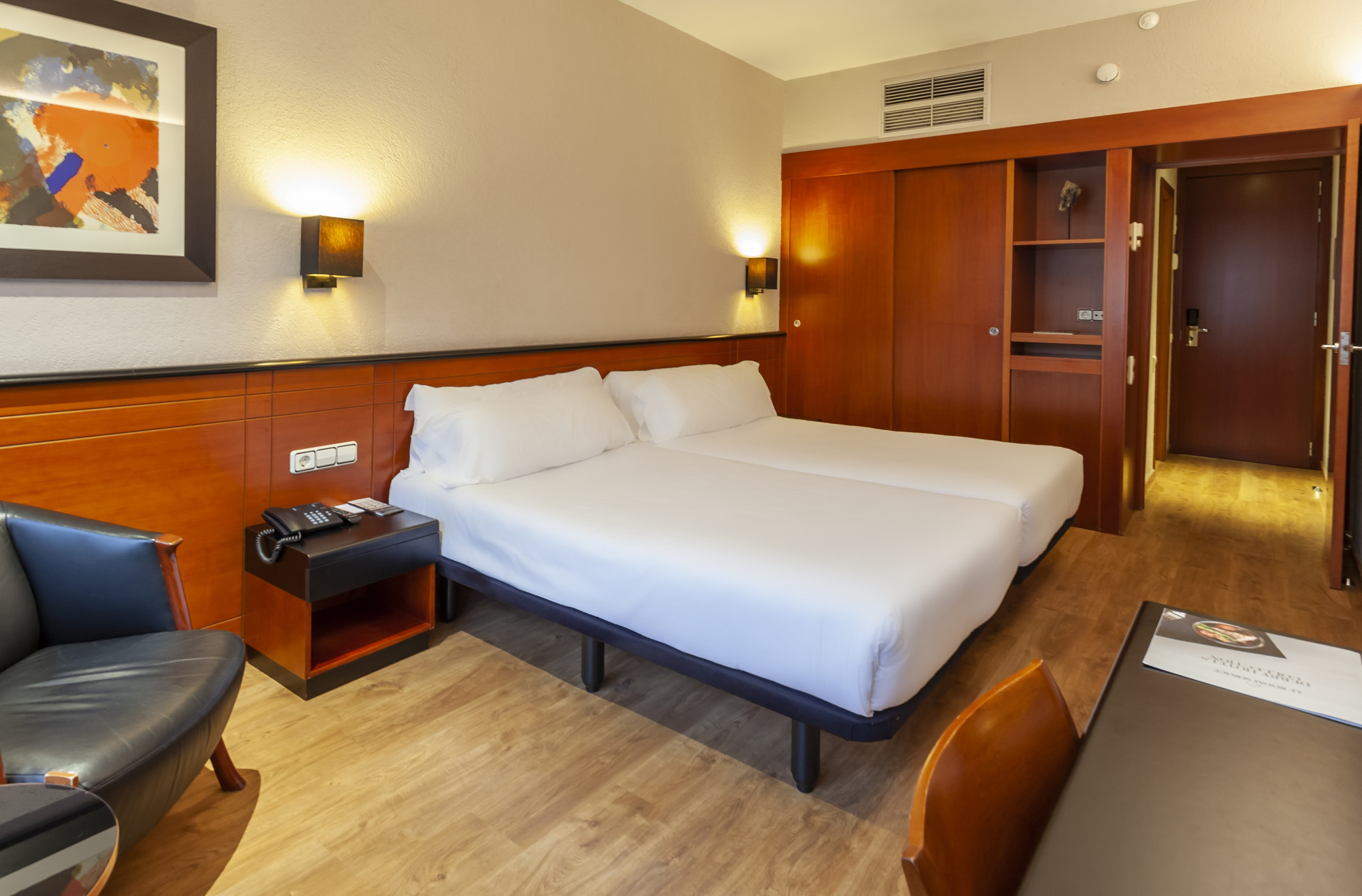 Se ve una habitación con una cama doble, mesitas laterales, sillón y armarios de madera.