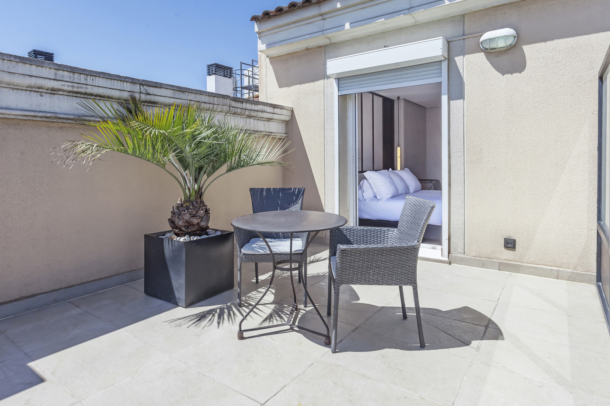 Se ve una terraza con suelo de baldosas, una mesa con sillas y una puerta abierta hacia una habitación.