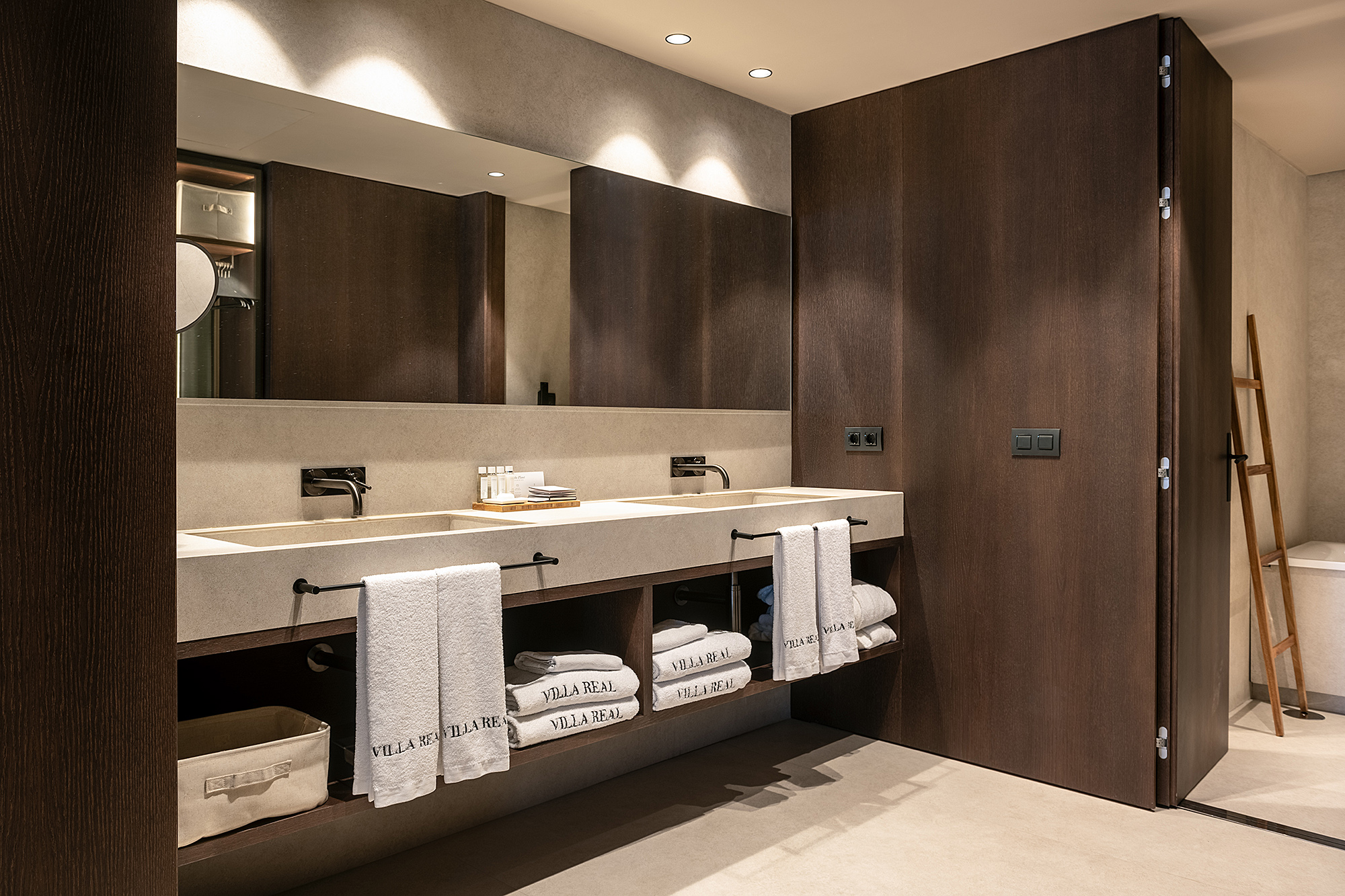 El baño muestra dos lavabos con encimeras claras, toallas dobladas y una ducha con mampara de vidrio.