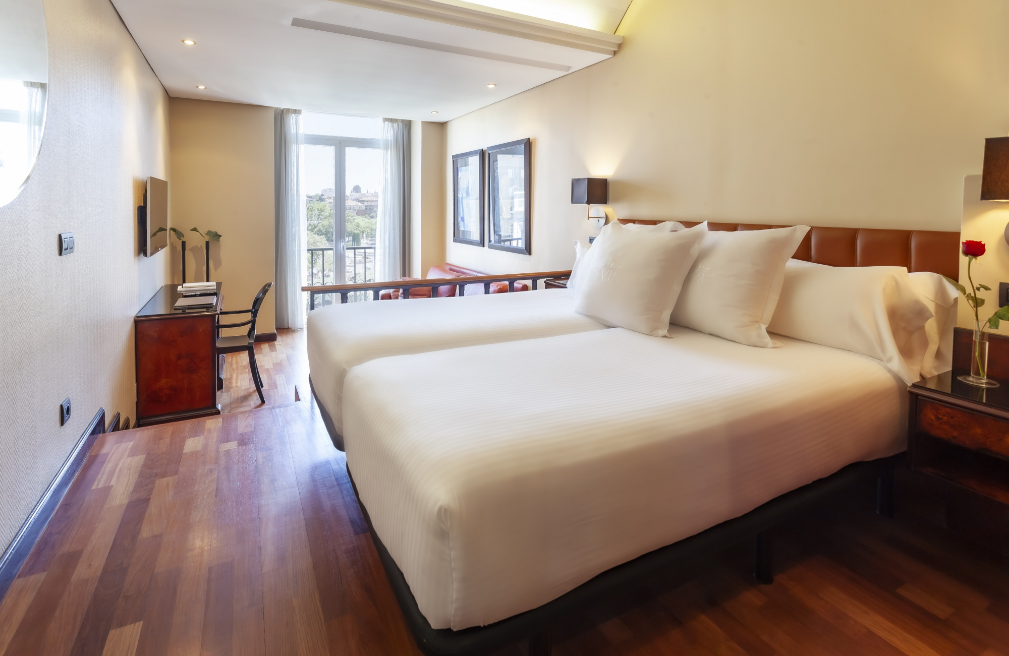 Se ve una cama doble con ropa de cama blanca y un ventanal con luz natural en una habitación moderna.