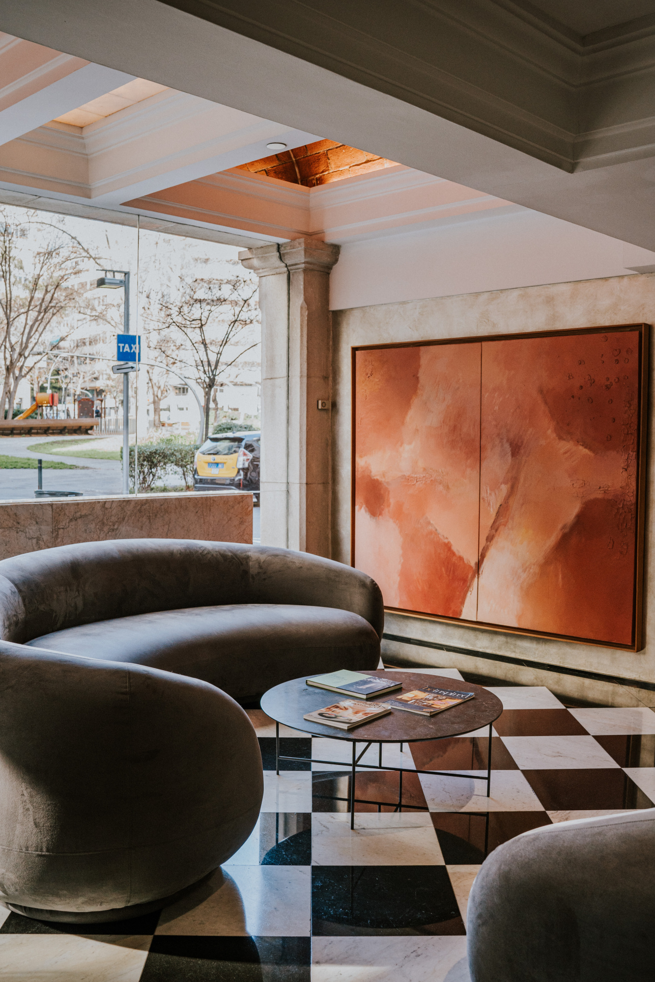 Se ve una zona de estar con sillones de tela, una mesa auxiliar y una pared con un cuadro grande.