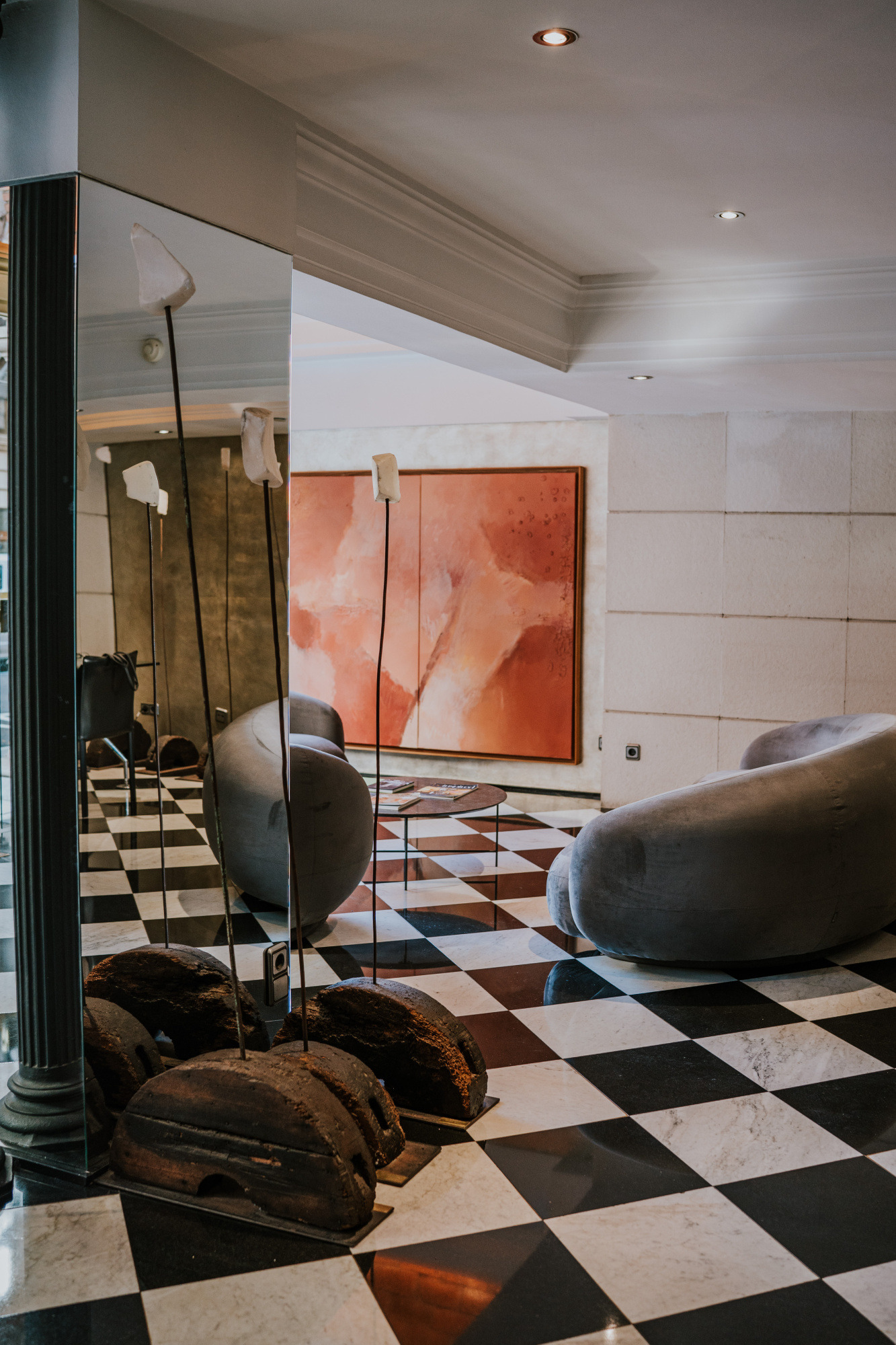 Se ve una zona de estar con sillones, suelo de baldosas en blanco y negro y una pared con arte abstracto.