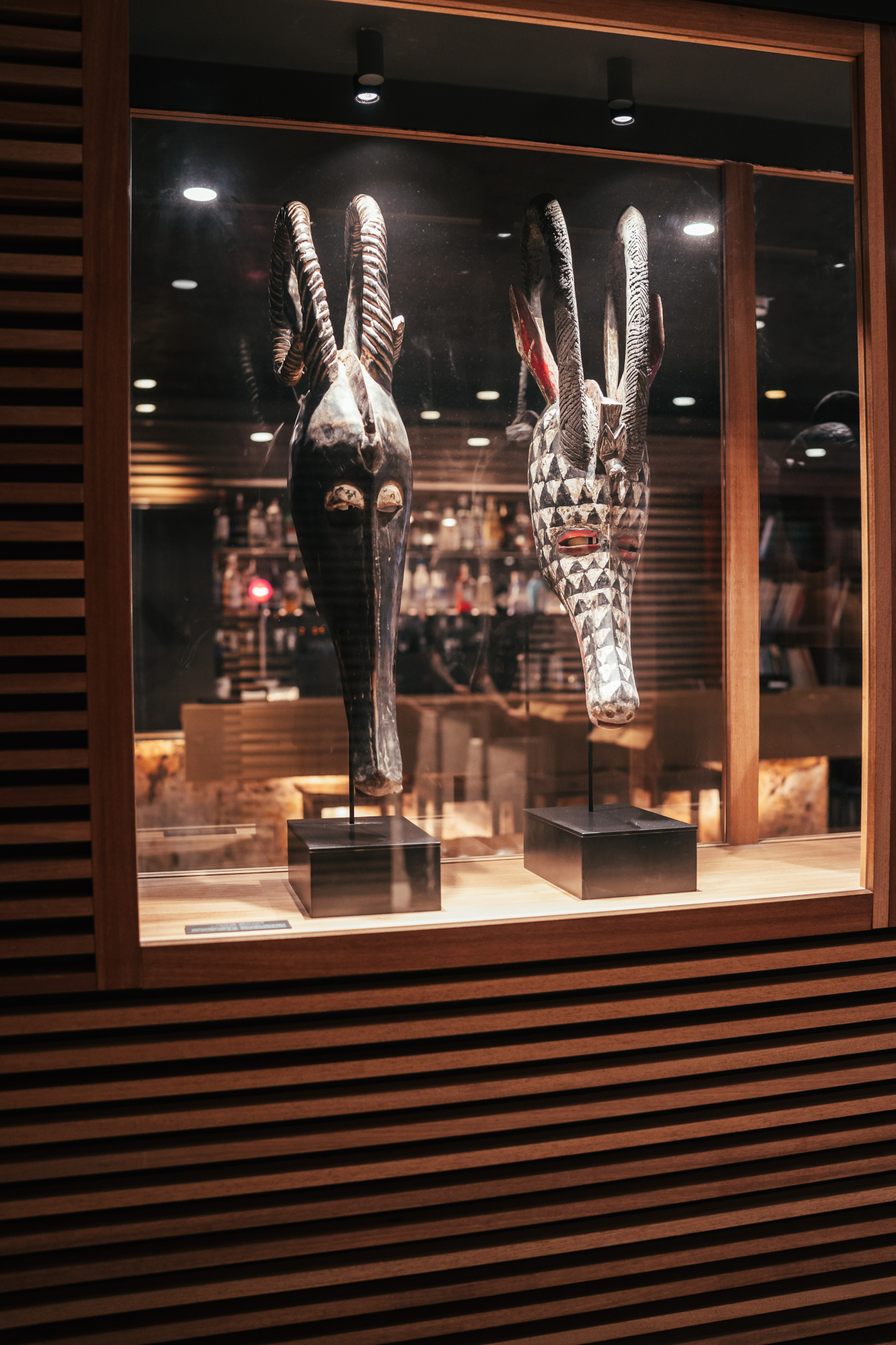 Se ve una vitrina con esculturas africanas y piezas decorativas iluminadas en un espacio interior.