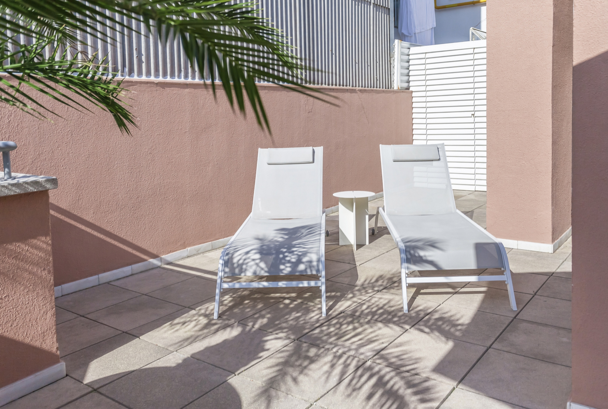 Se ve una terraza con dos tumbonas blancas y una mesa pequeña sobre suelo de baldosas.