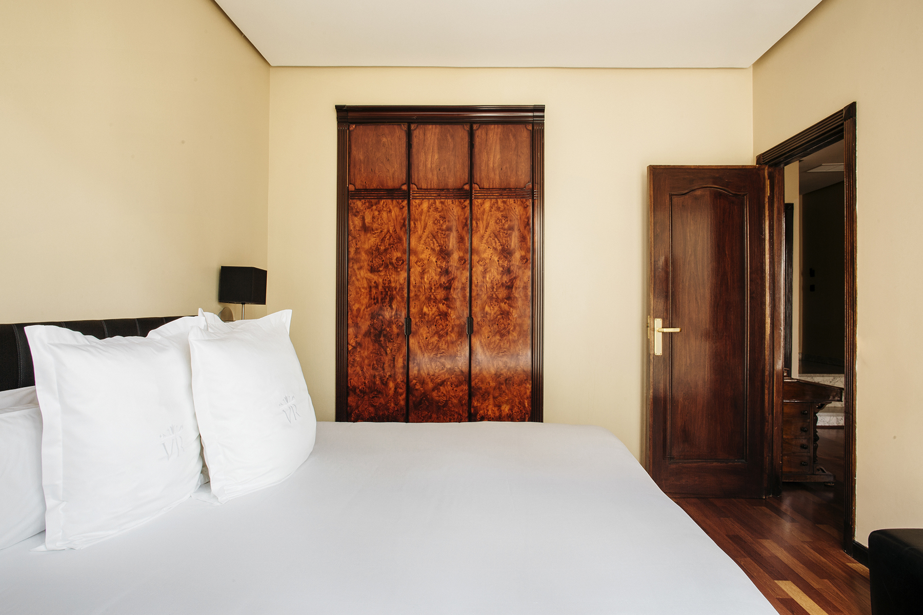 Se ve una cama doble con almohadas blancas y una puerta de madera en un dormitorio.