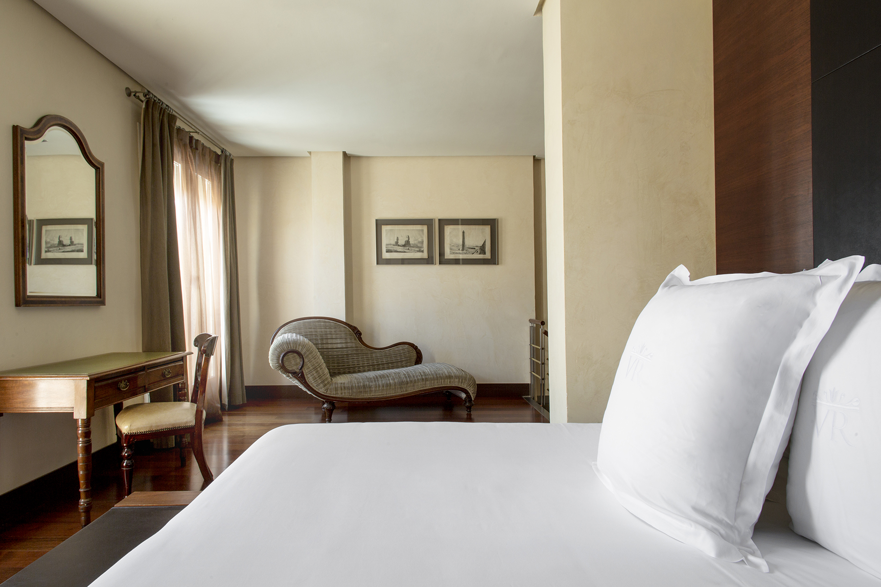 Se ve una cama doble con ropa de cama blanca y una zona de estar con sillón y mesa auxiliar.