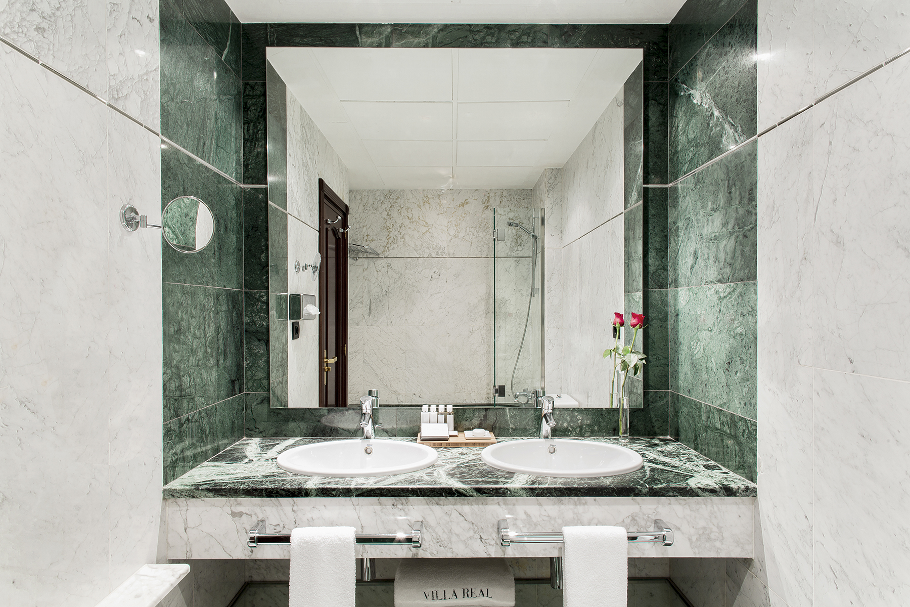 El baño muestra un doble lavabo sobre encimera de mármol, grifería cromada y dos toallas dobladas.