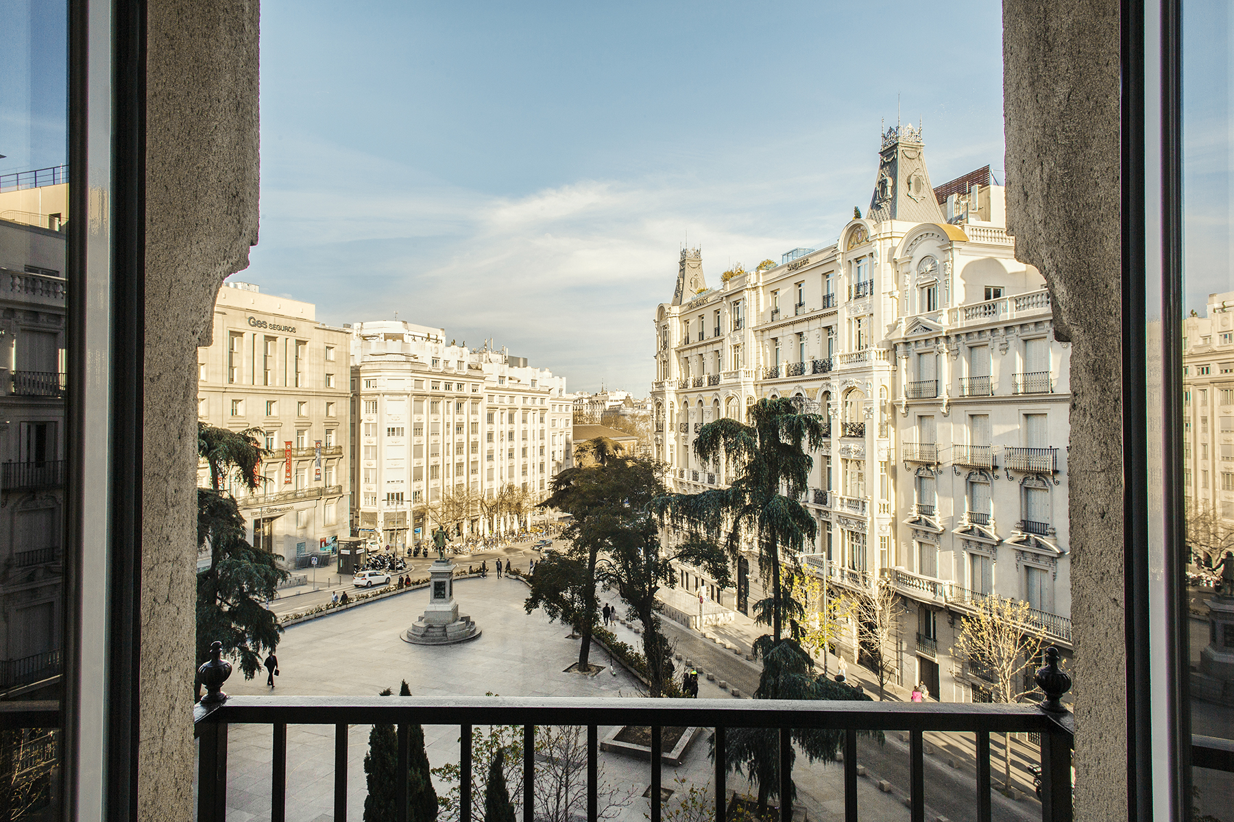 Desde un balcón se ve una avenida con edificios altos y árboles a lo largo de la calle.