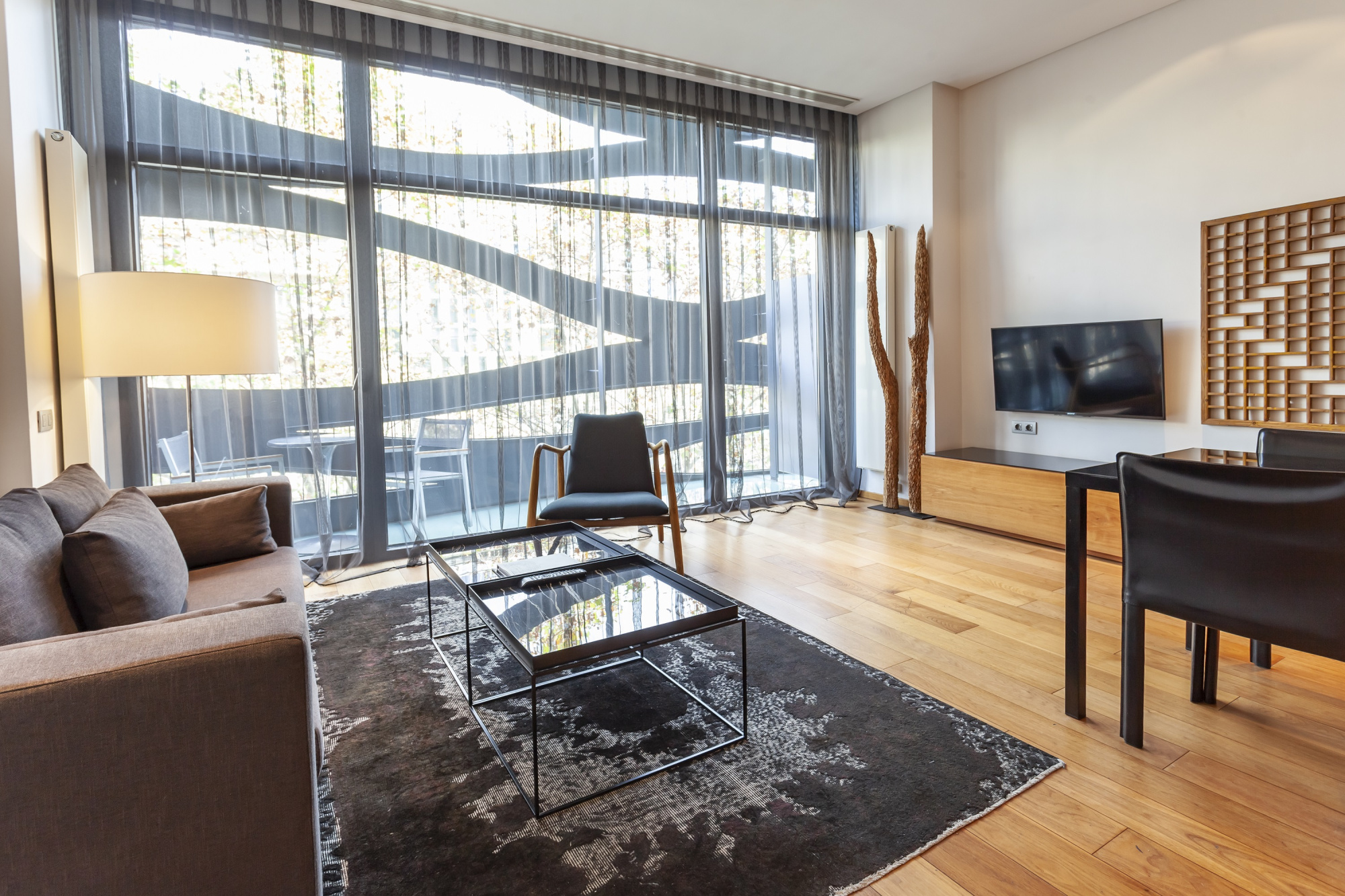 Un salón moderno con sofá, mesa de centro, alfombra y un gran ventanal con cortinas.