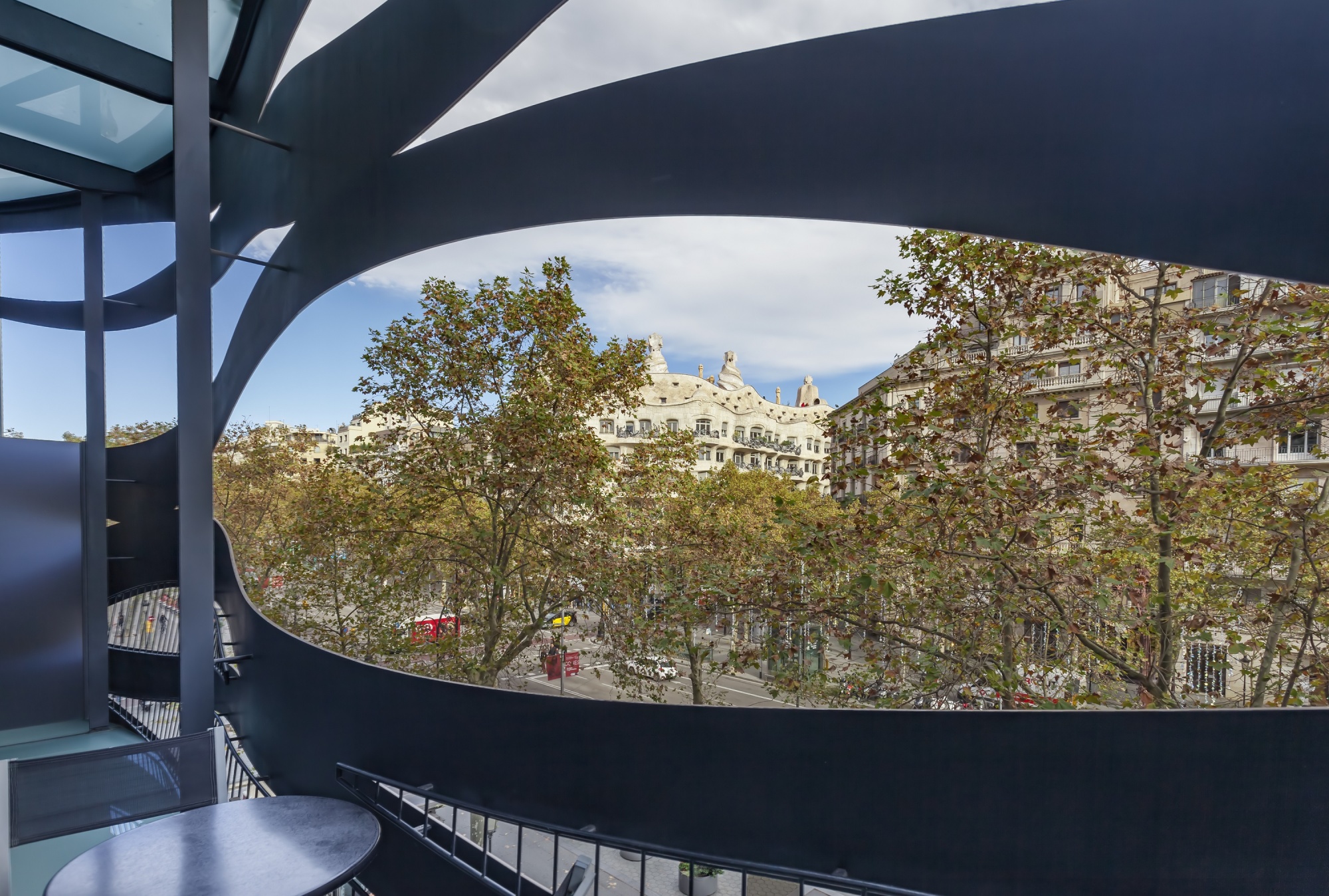 Se ve una terraza con barandilla y una ventana arqueada abierta al exterior con edificios al fondo.