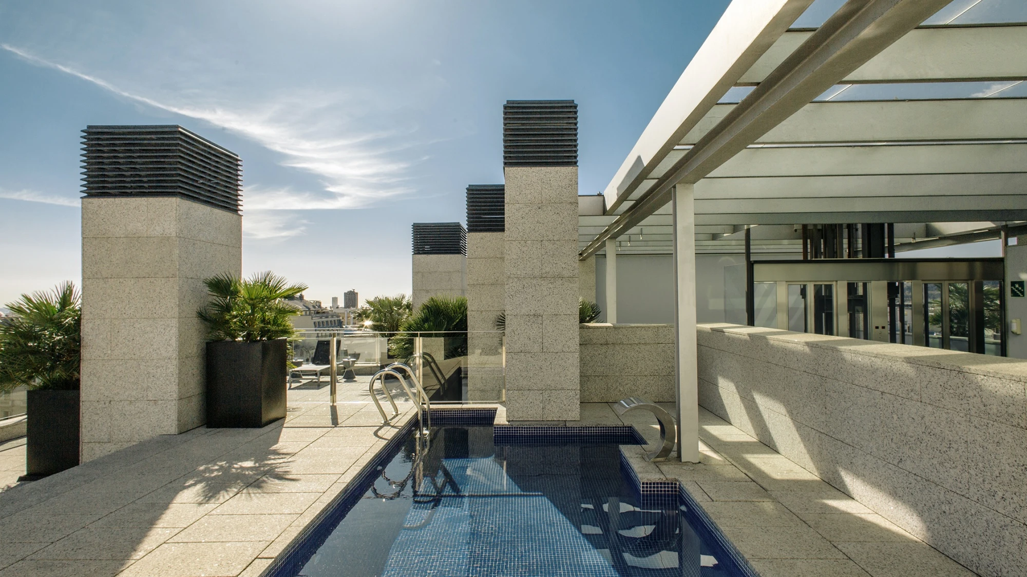 Se ve una terraza al aire libre con una piscina pequeña y tumbonas junto a una estructura acristalada.