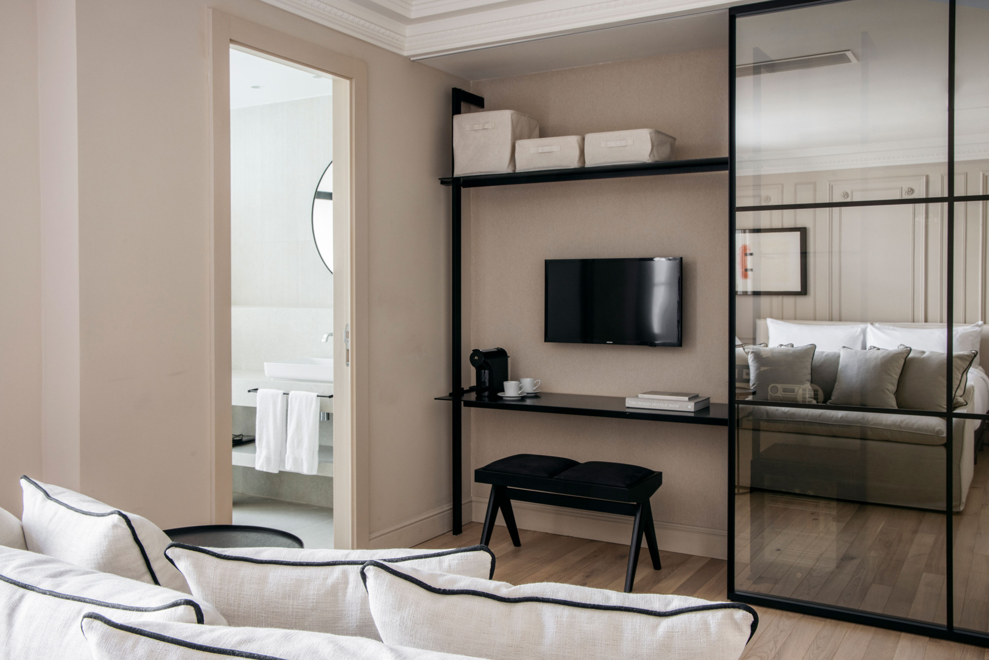 Se ve una cama con ropa de cama clara y una zona de estar con TV y escritorio junto a una ventana.