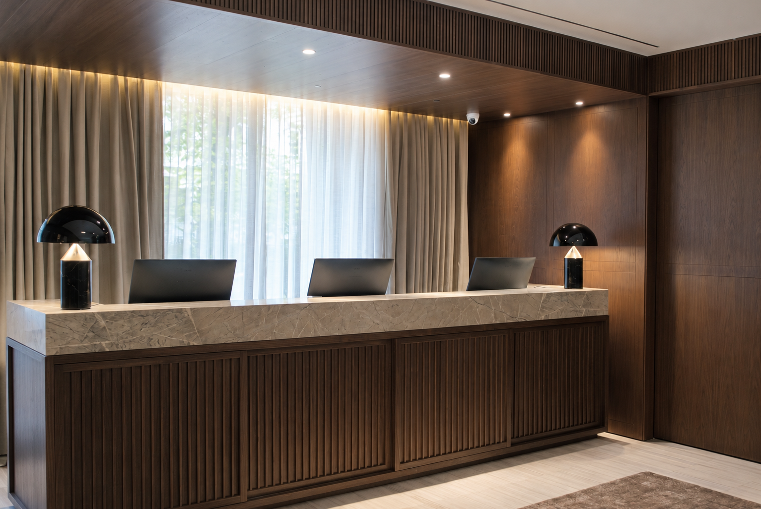Se ve un mostrador de recepción de madera con dos lámparas y cortinas claras detrás.