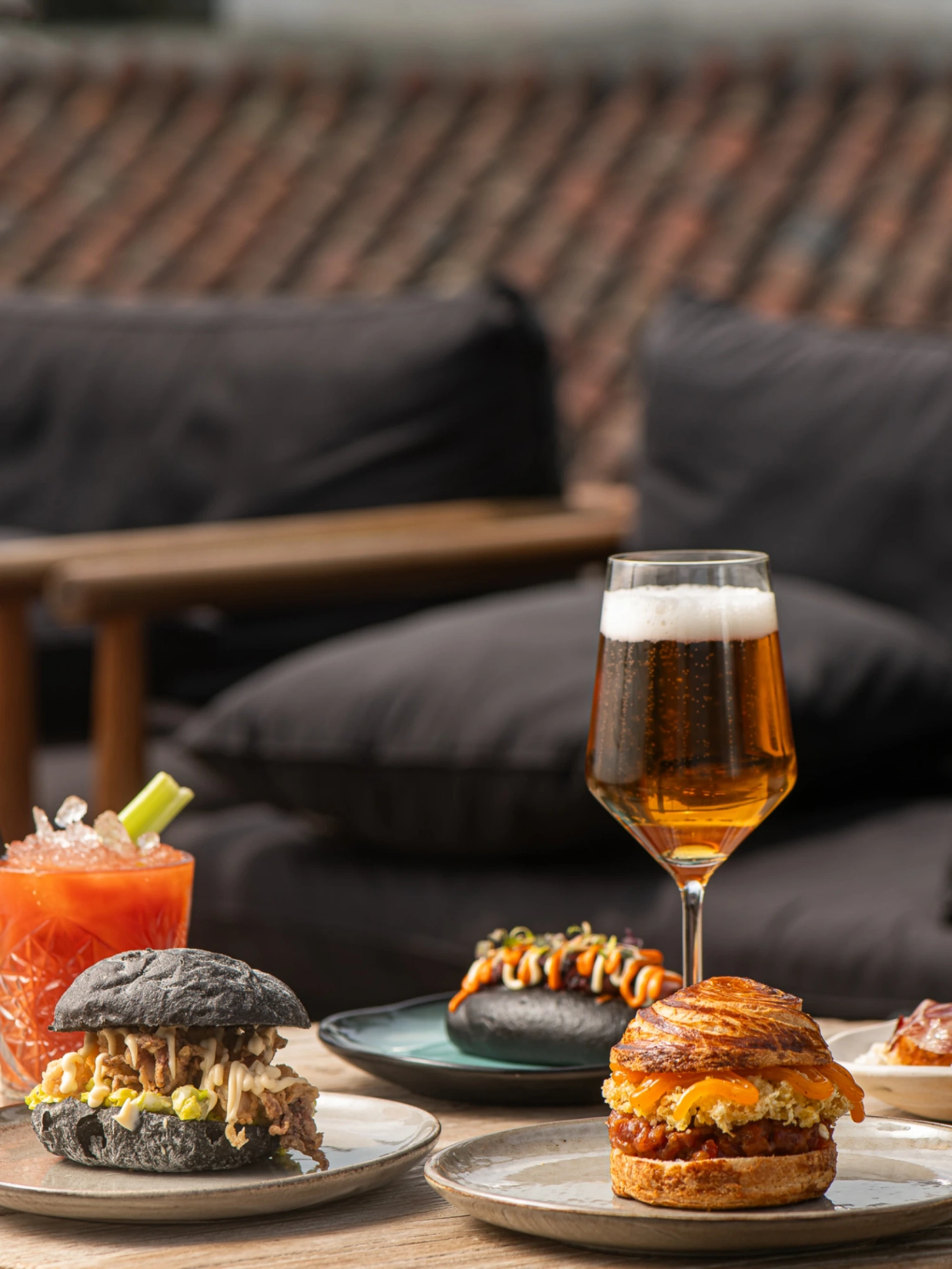 Se ven varias hamburguesas y vasos con cerveza sobre una mesa en un área de comedor al aire libre.